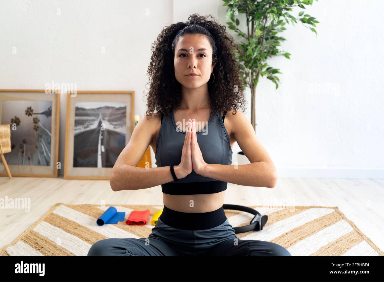 Curly haired woman with hands clasped doing relaxation exercise at home Stock Photo