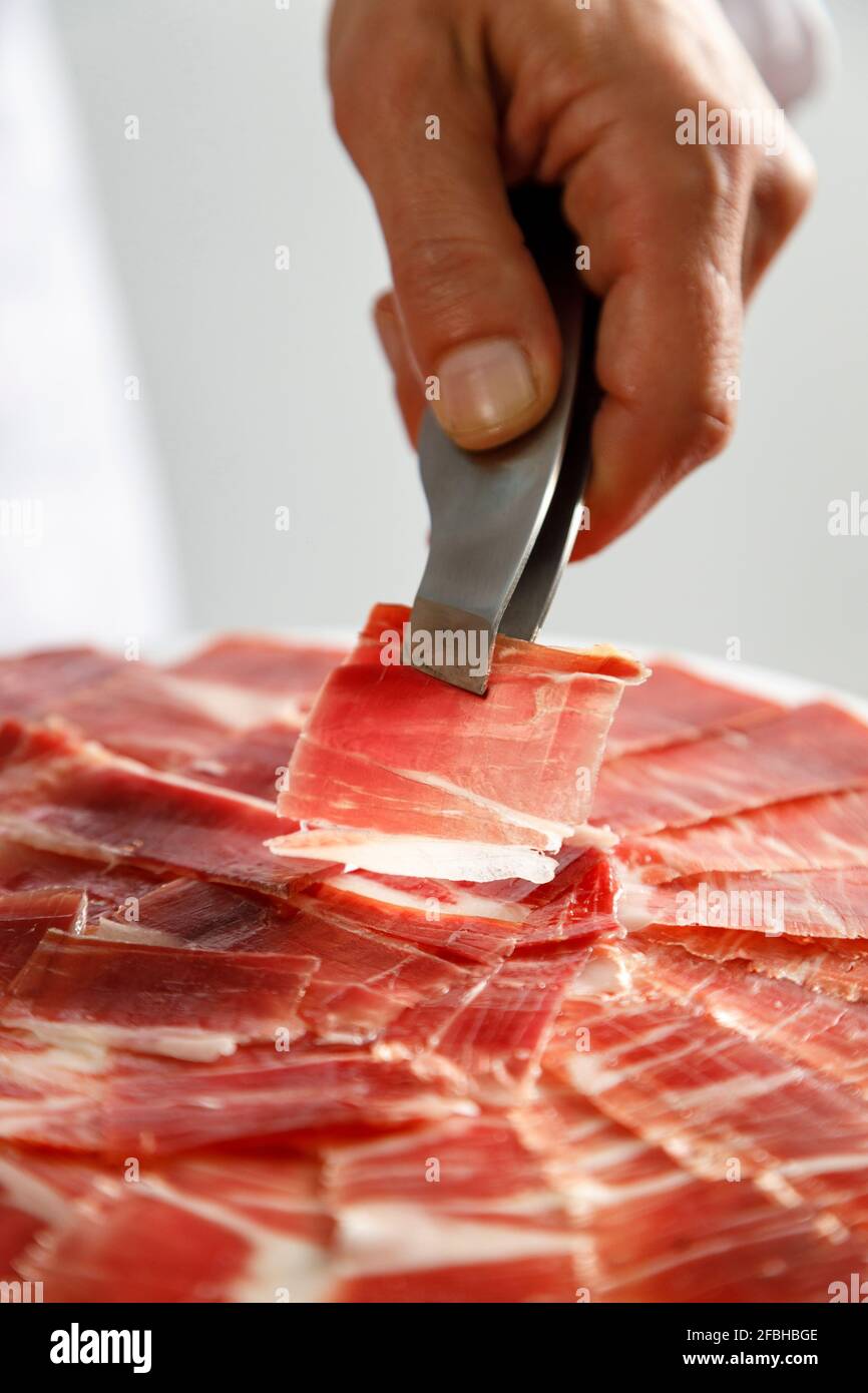 Butcher hand holding Iberian ham slice with tong Stock Photo