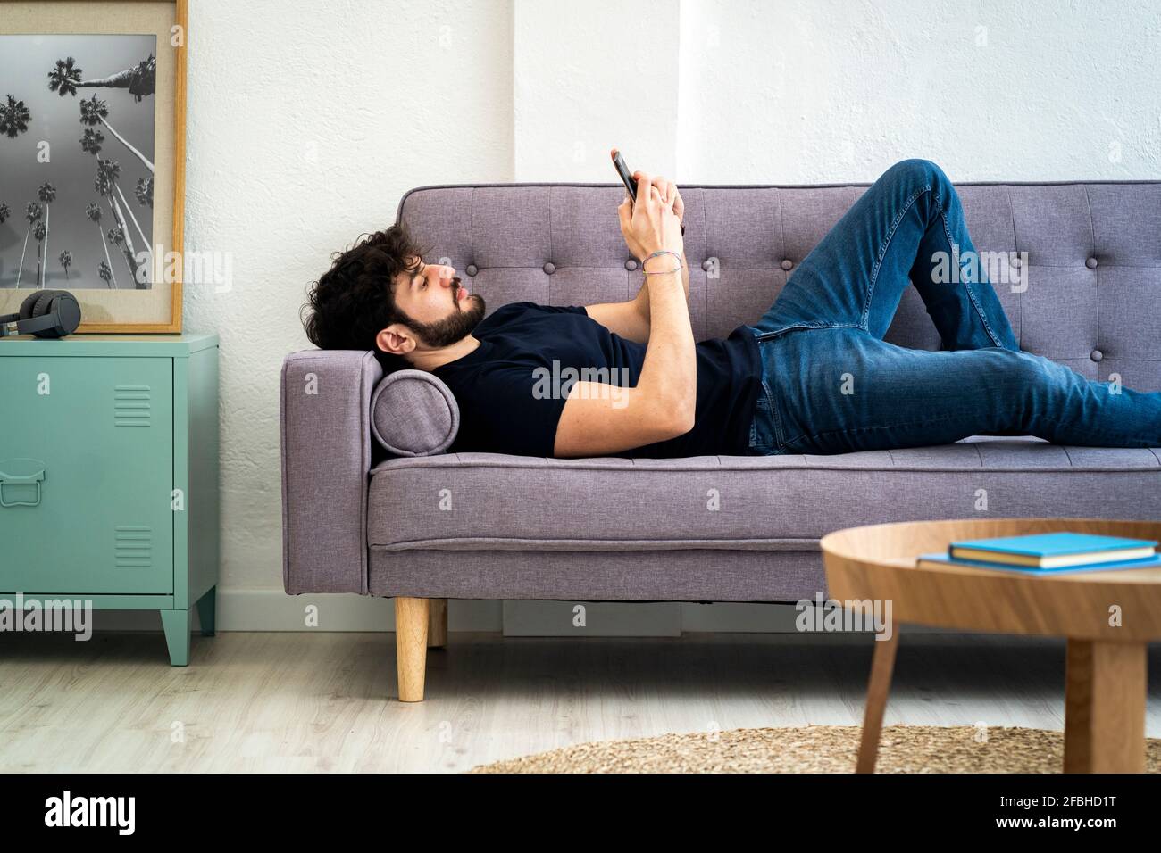 Relaxed young man using smart phone while lying on sofa at home Stock Photo