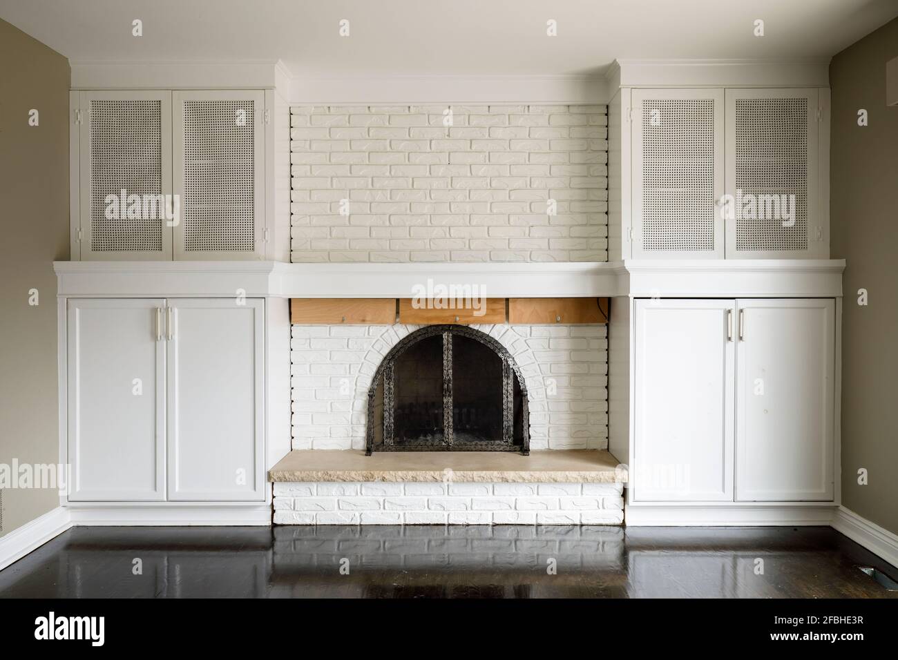A brick fireplace painted white with built in cabinets on either side ...