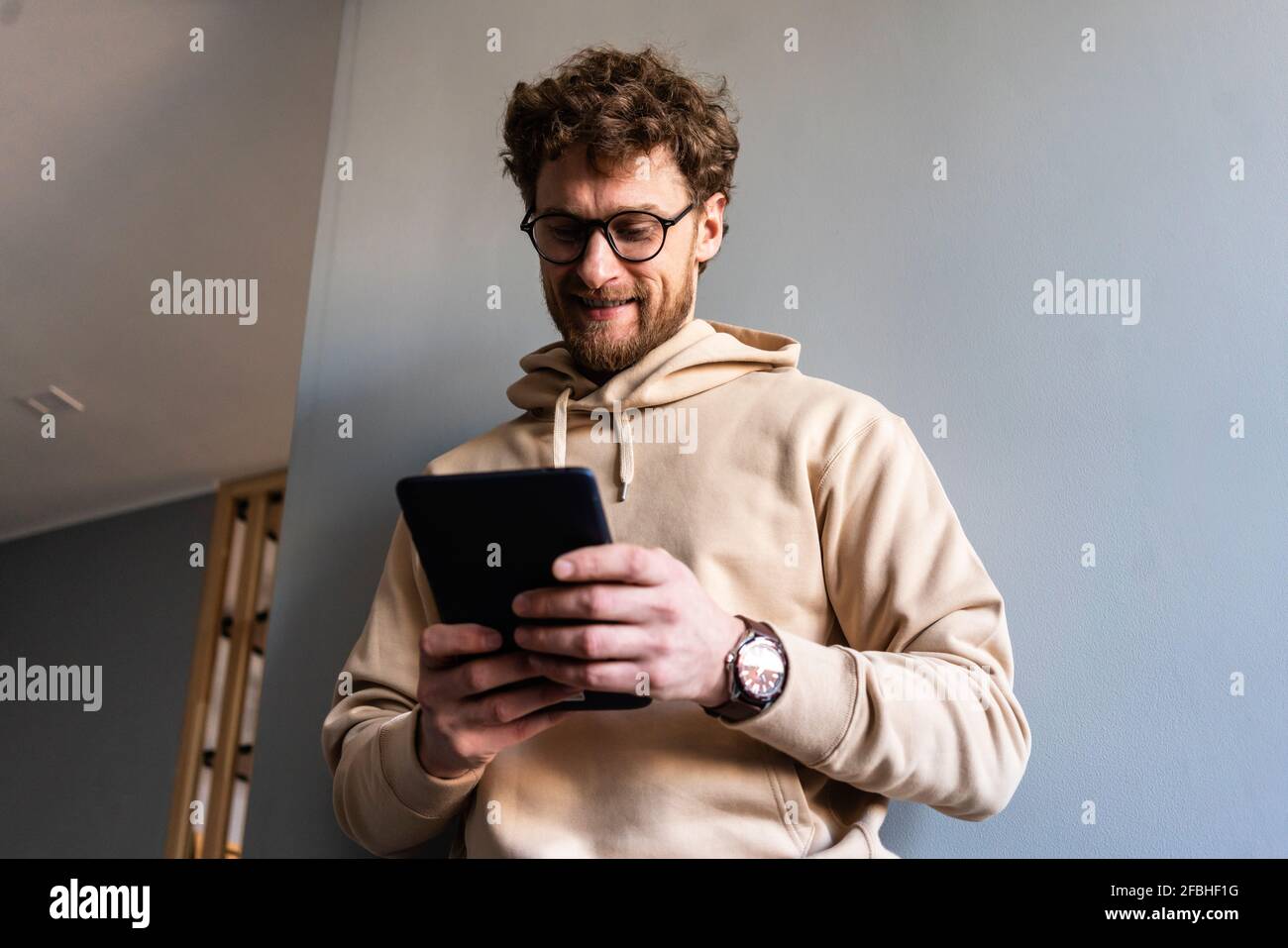 Smiling man wearing eyeglasses using digital tablet at home Stock Photo