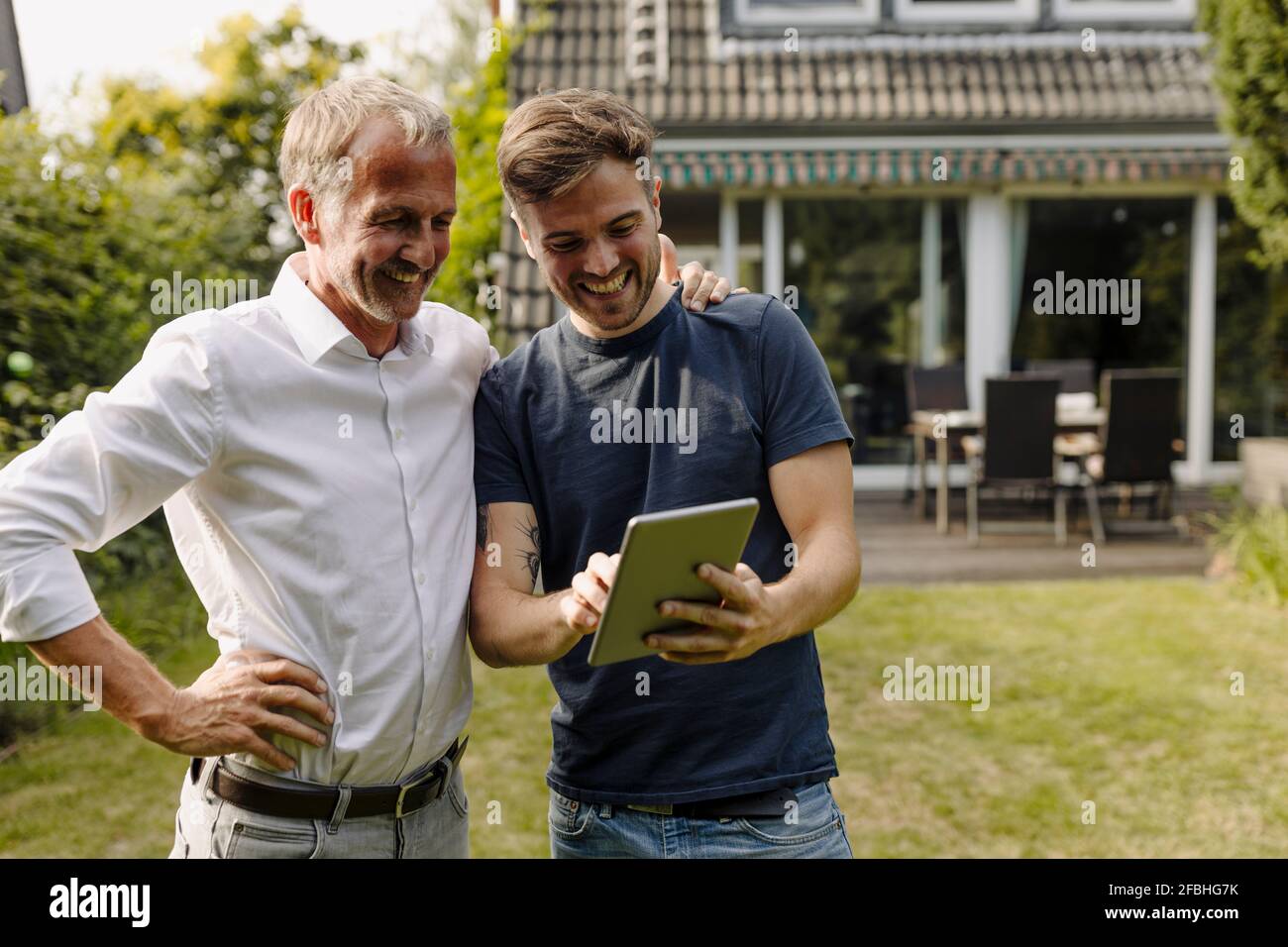 Happy son using digital tablet while standing by father in backyard Stock Photo