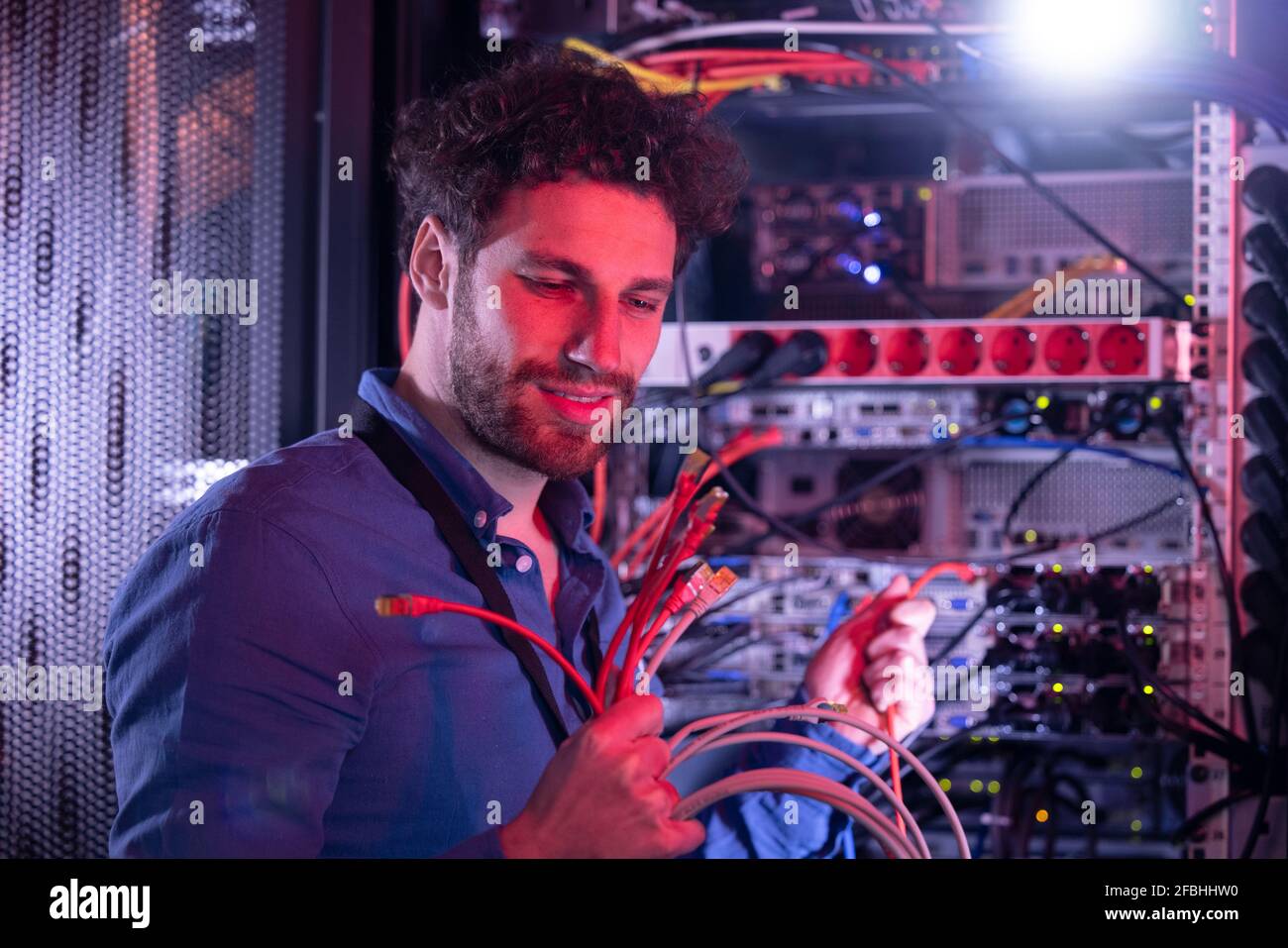 Male IT technician looking at patch cord cables while standing by server rack Stock Photo