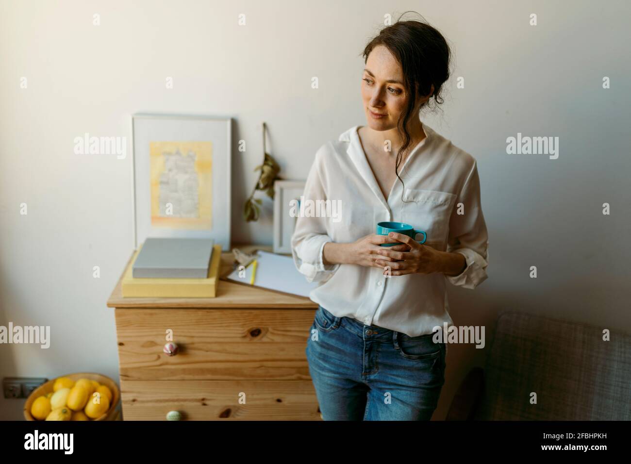 Beautiful female brunette leaning on side table while looking away at home Stock Photo