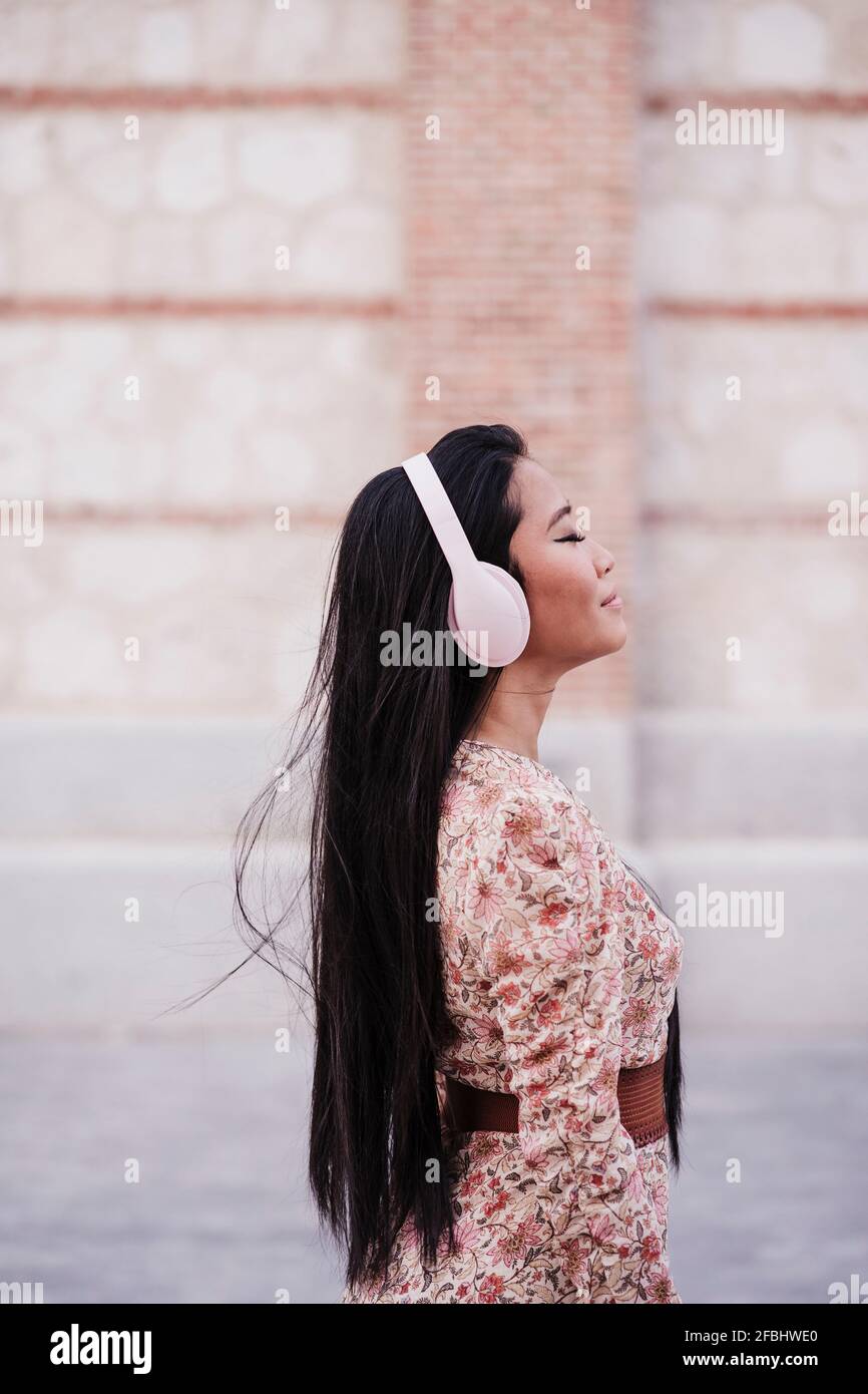 Woman with long hair wearing headphones while standing near wall Stock Photo