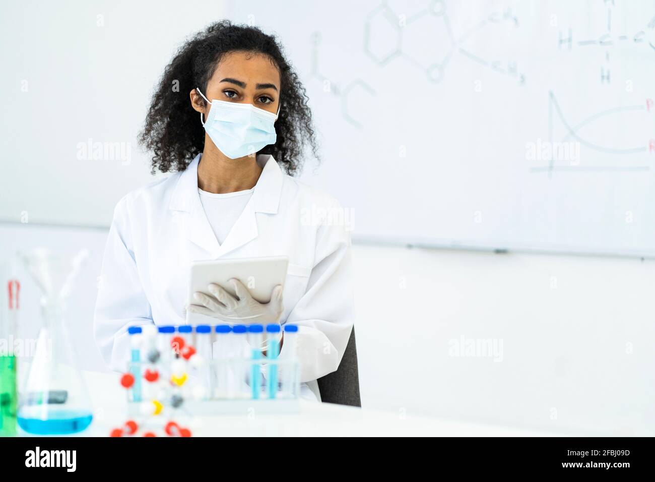 Young female researcher with digital tablet in laboratory during COVID-19 Stock Photo