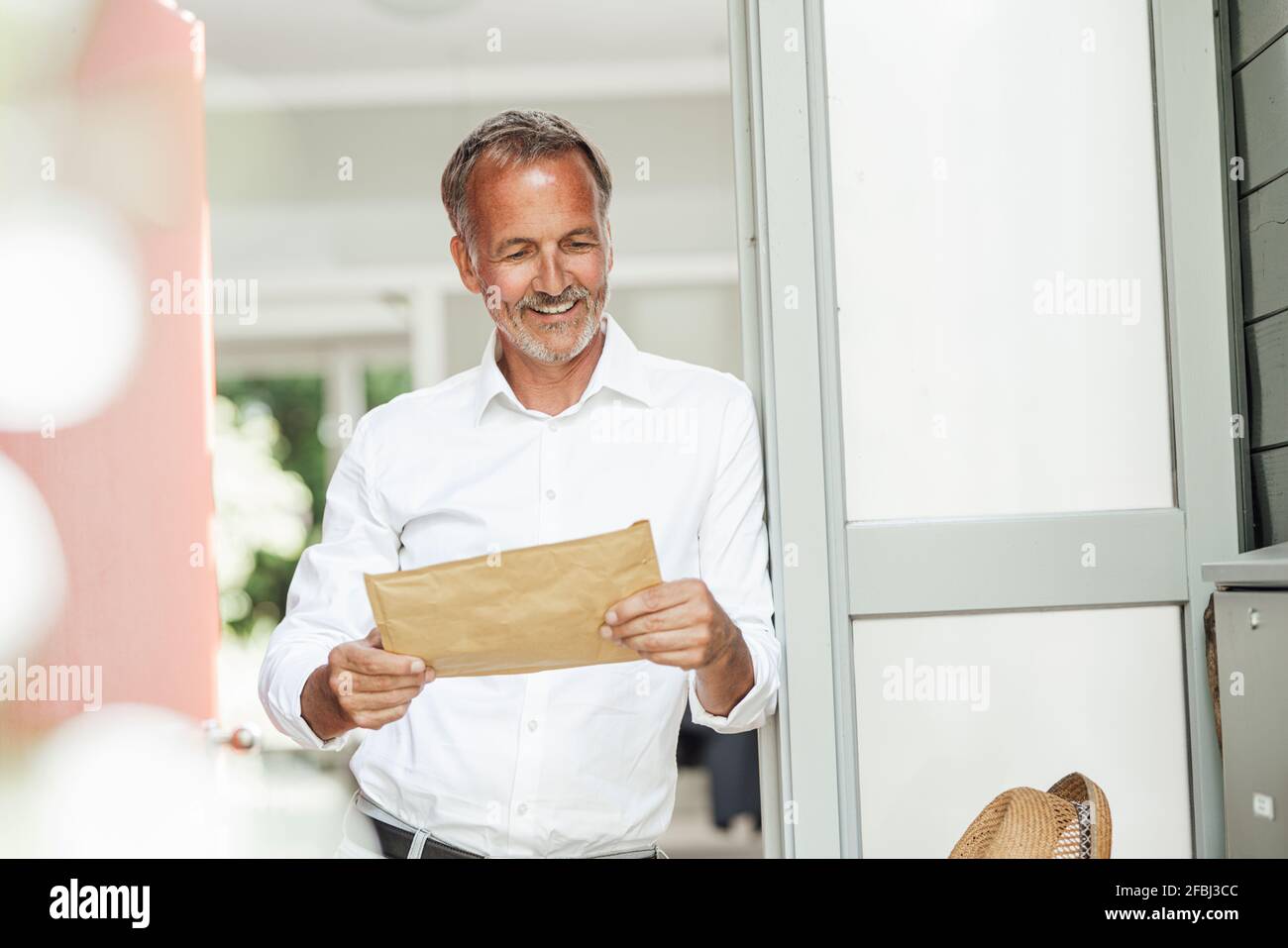 Smiling mature man looking at parcel held at front door Stock Photo