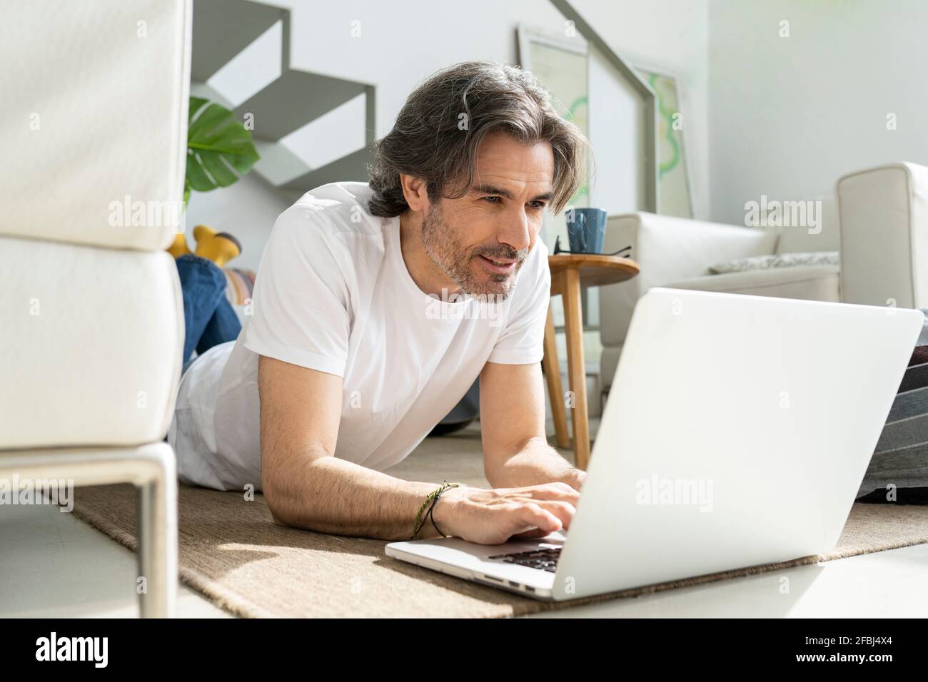 Man using laptop while lying on floor at home Stock Photo
