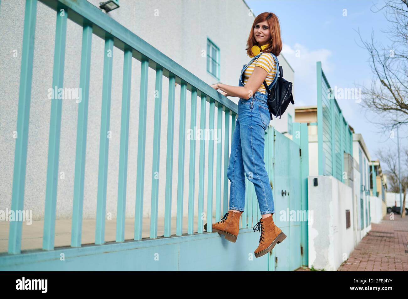 Redhead woman in bib overall climbing on turquoise blue railing Stock Photo