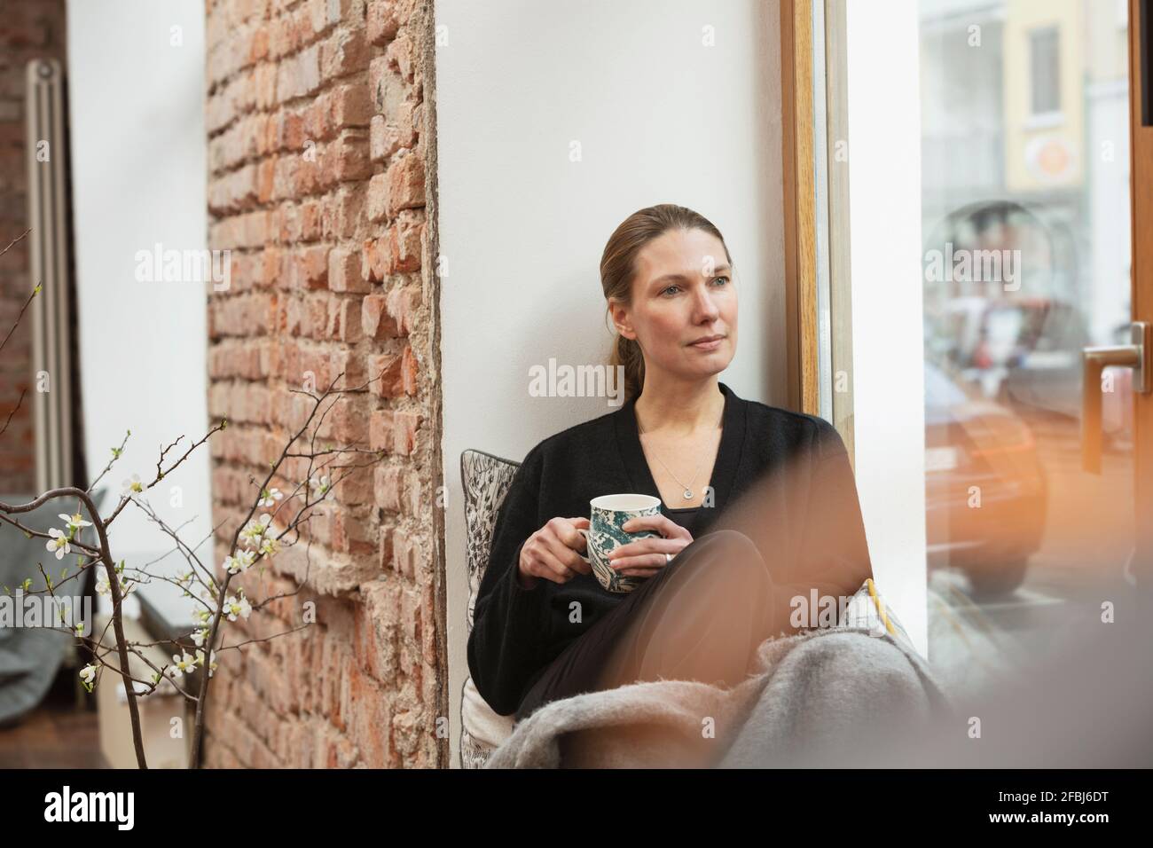 thoughtful-female-professional-with-tea-mug-sitting-by-window-at-home