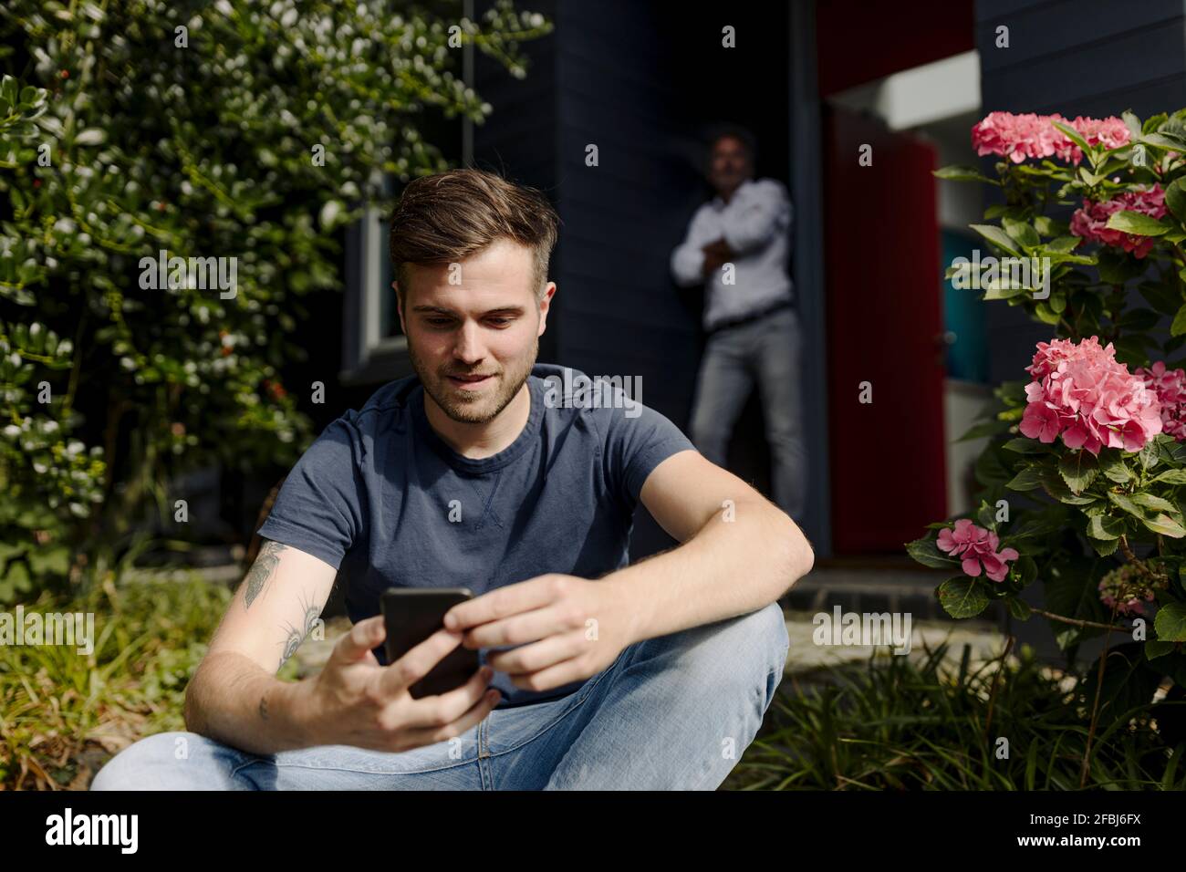 Son using smart phone while father leaning on wall Stock Photo