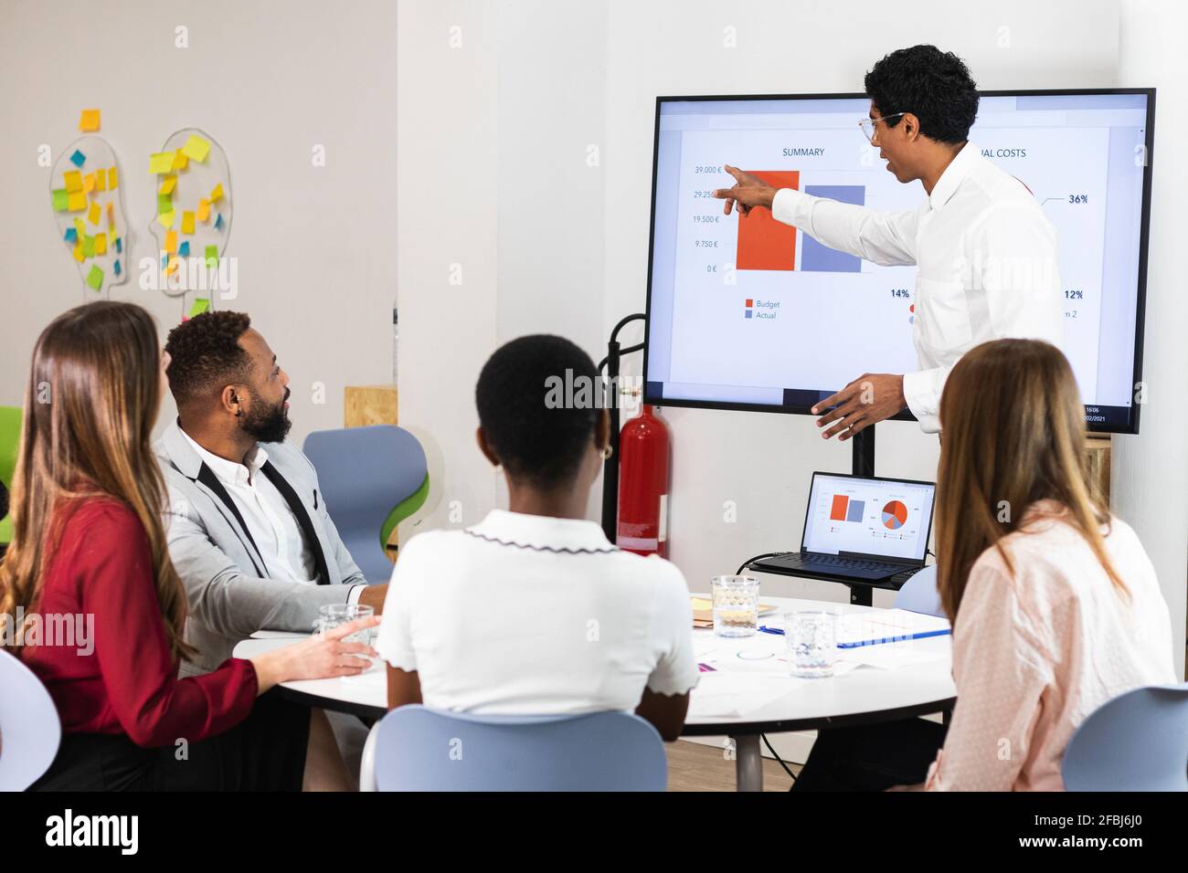 Businessman explaining plan over television to colleagues at office Stock Photo