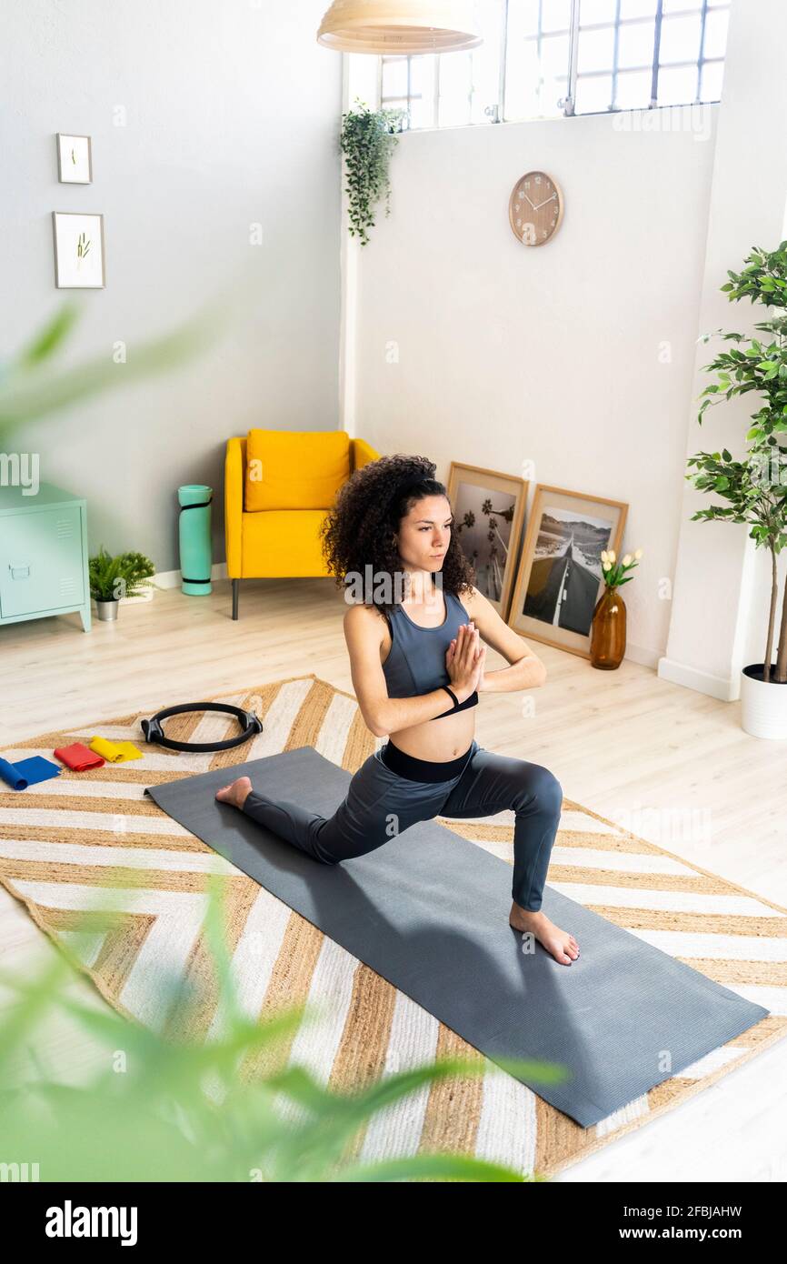 Woman in sports clothing doing sun salutation in living room Stock Photo