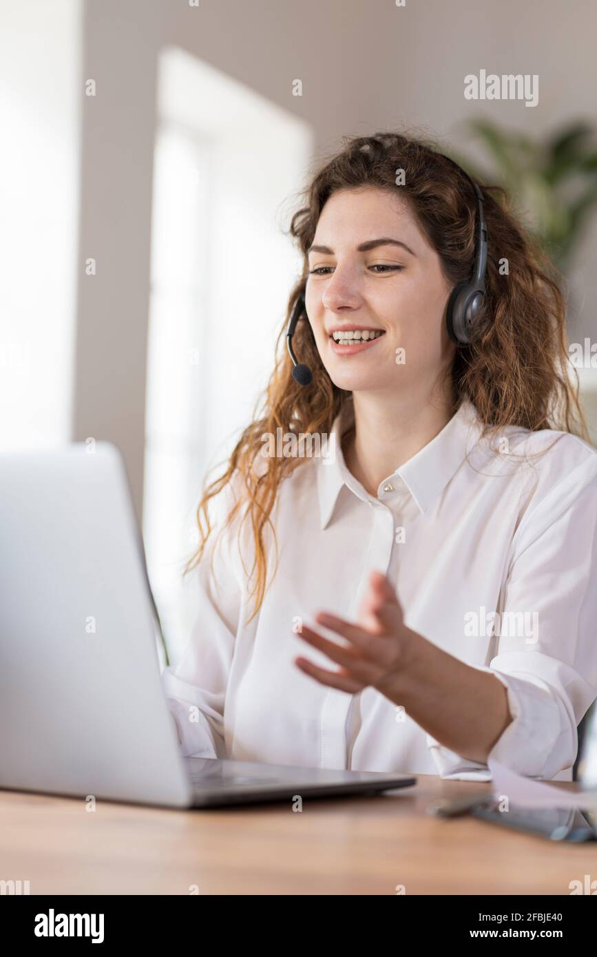 Contented female customer service representative with headphones explaining to client headphones at desk in home office Stock Photo