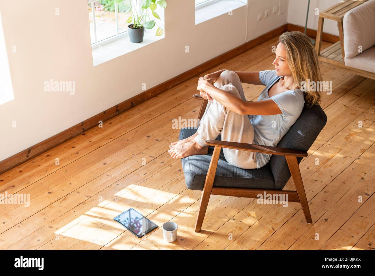 Woman hugging knees while contemplating at home Stock Photo