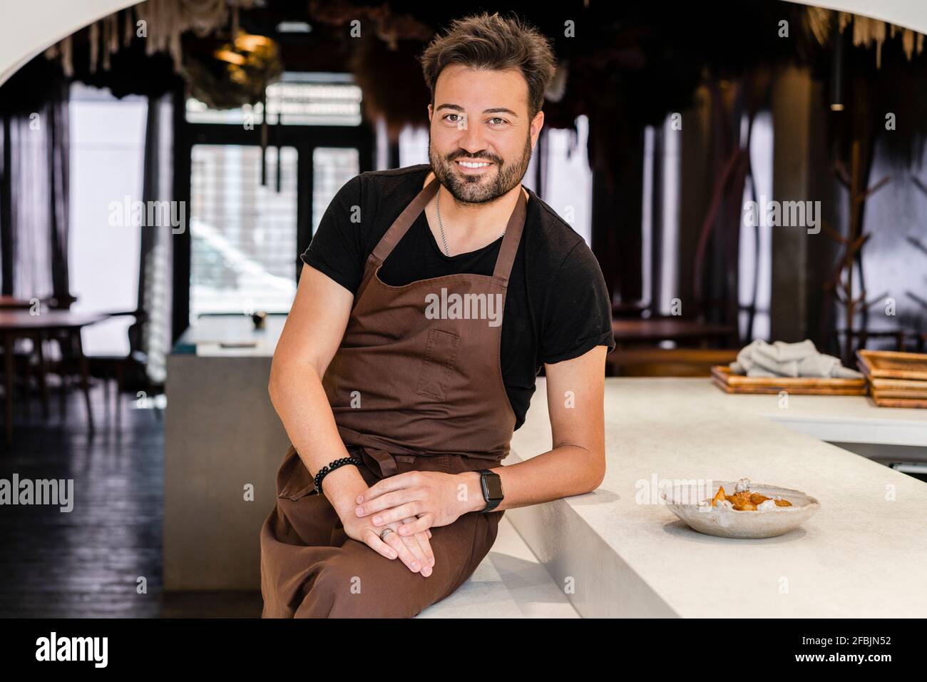 Smiling chef leaning while sitting by restaurant counter Stock Photo