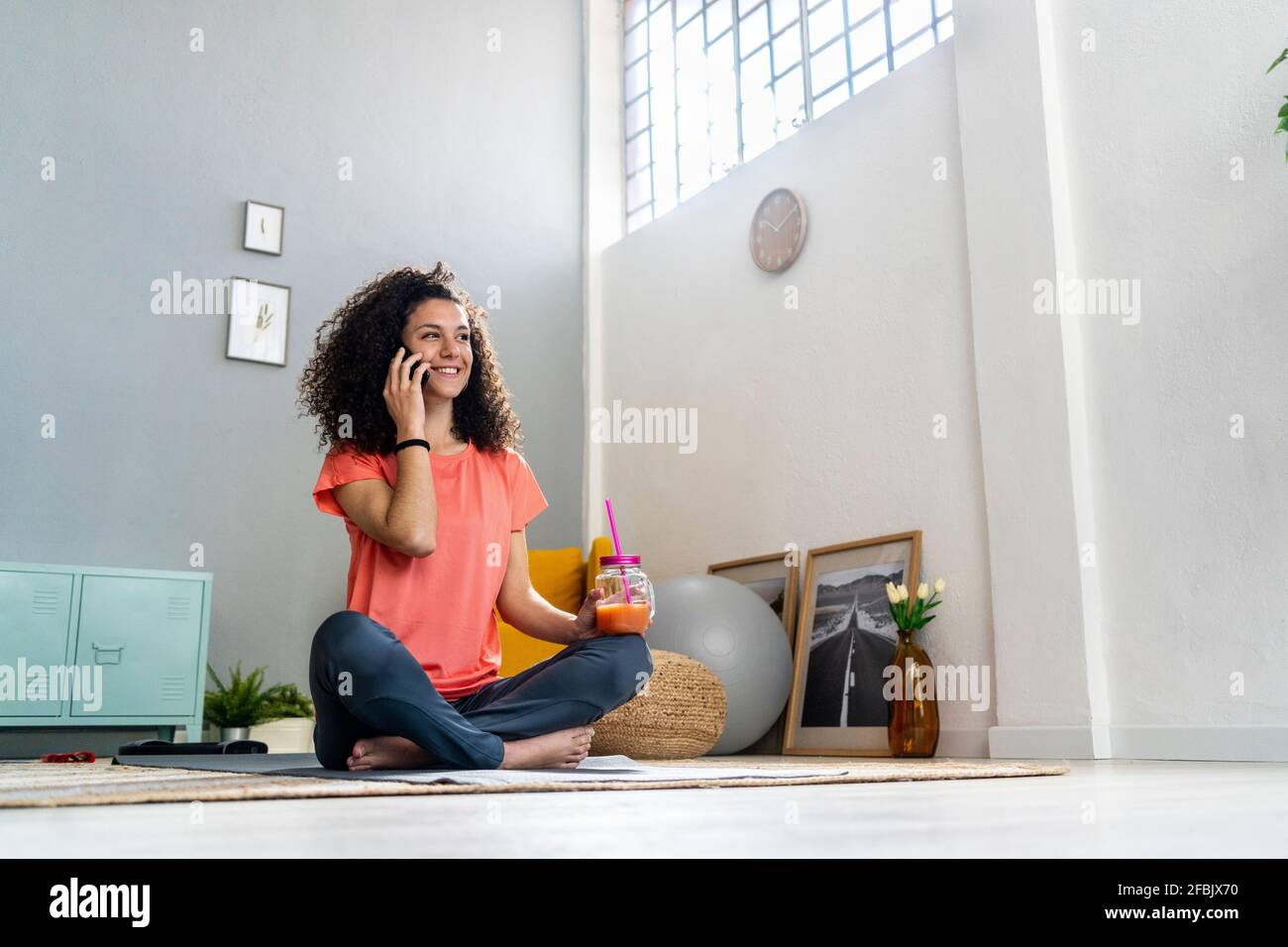 Smiling woman talking on mobile phone while holding juice jar at home Stock Photo