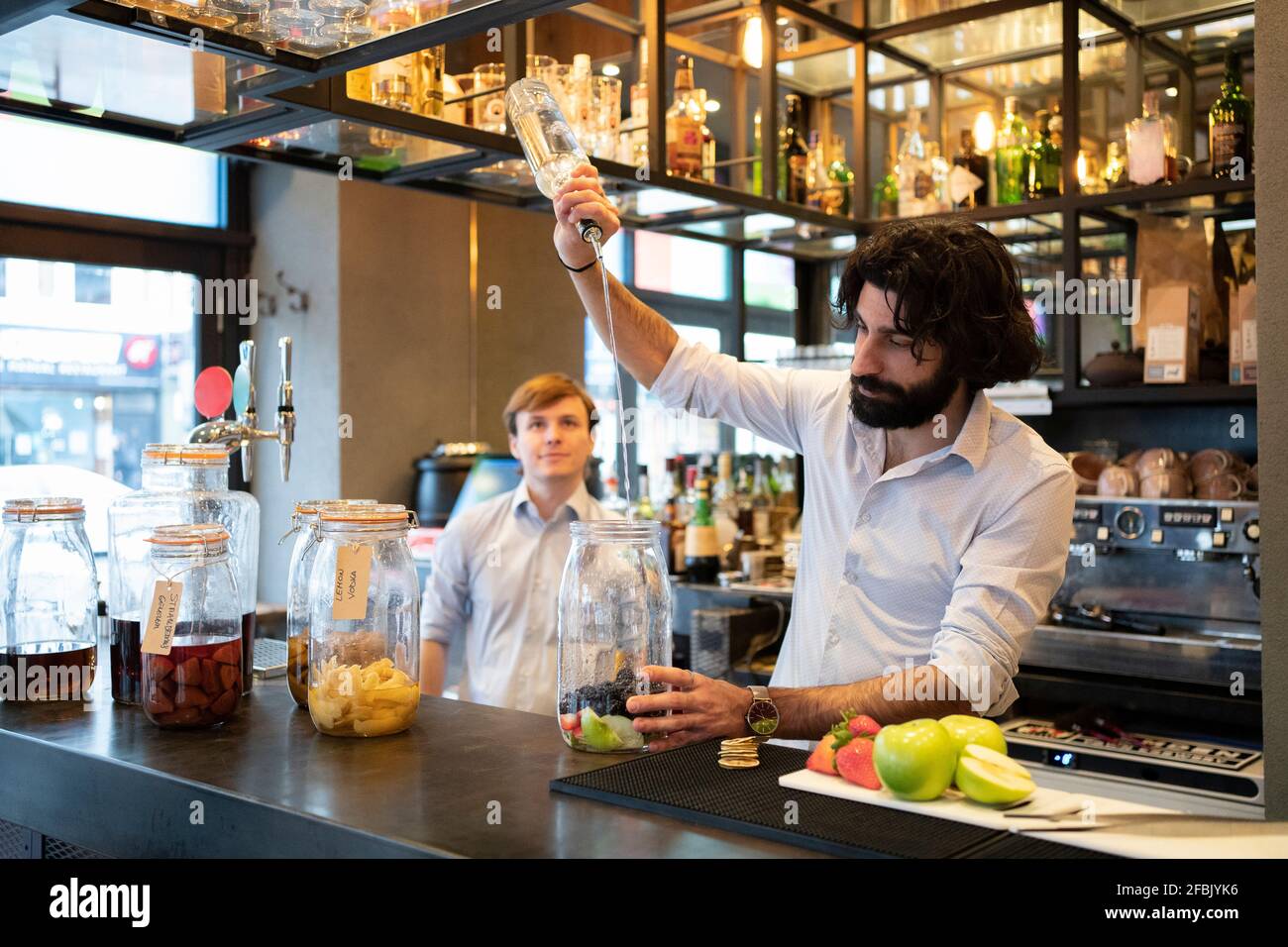 Male bartender pouring alcohol in fruit jar at bar counter Stock Photo