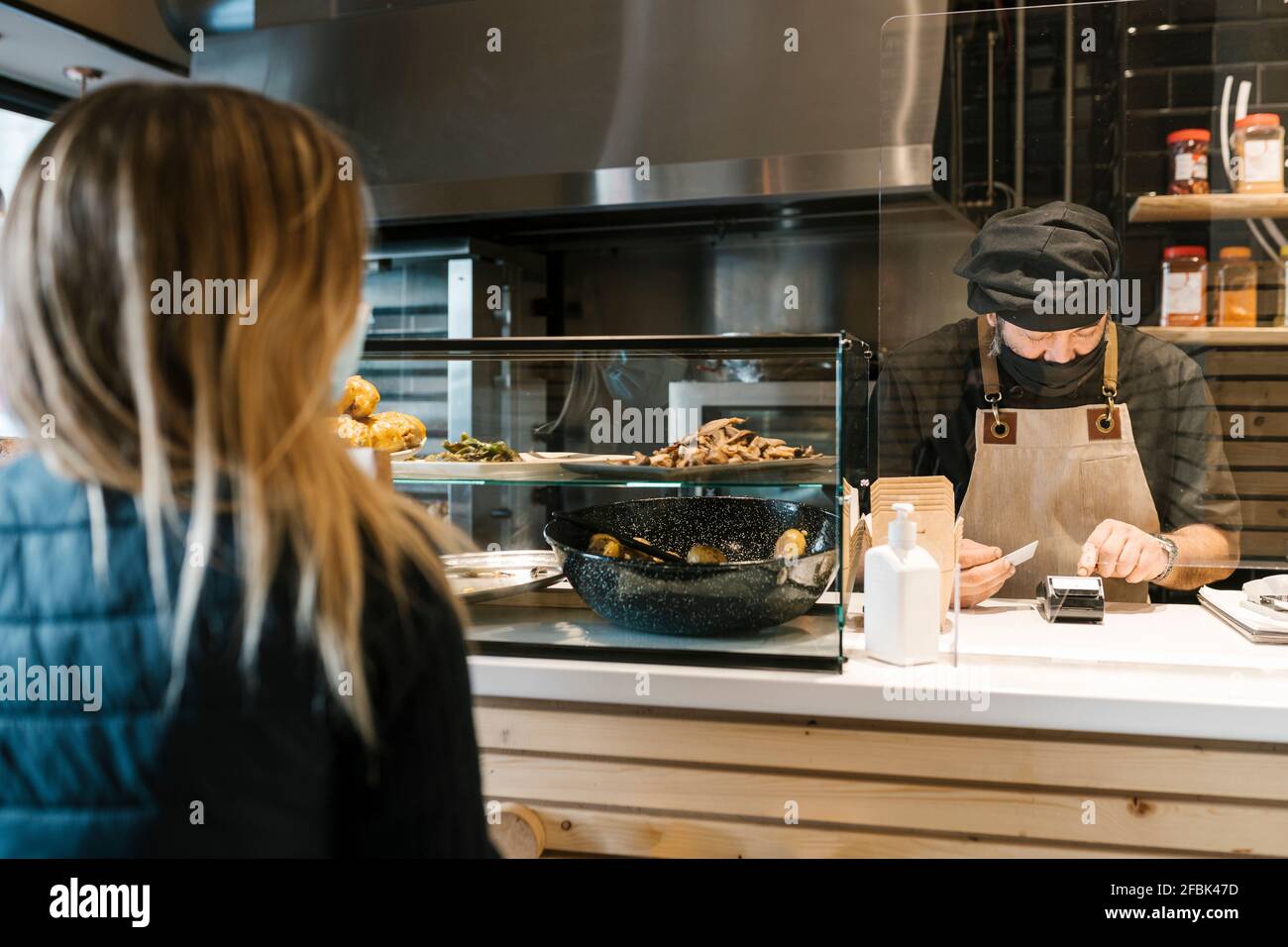 Male cashier using credit card reader machine while female customer waiting in restaurant Stock Photo