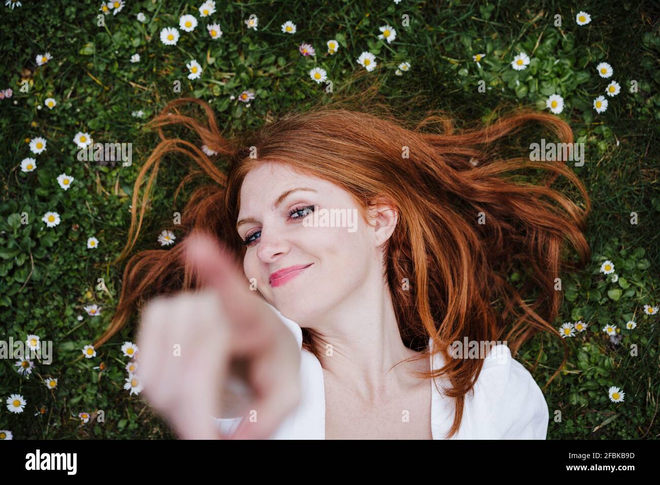 Smiling young woman pointing while lying on grass Stock Photo