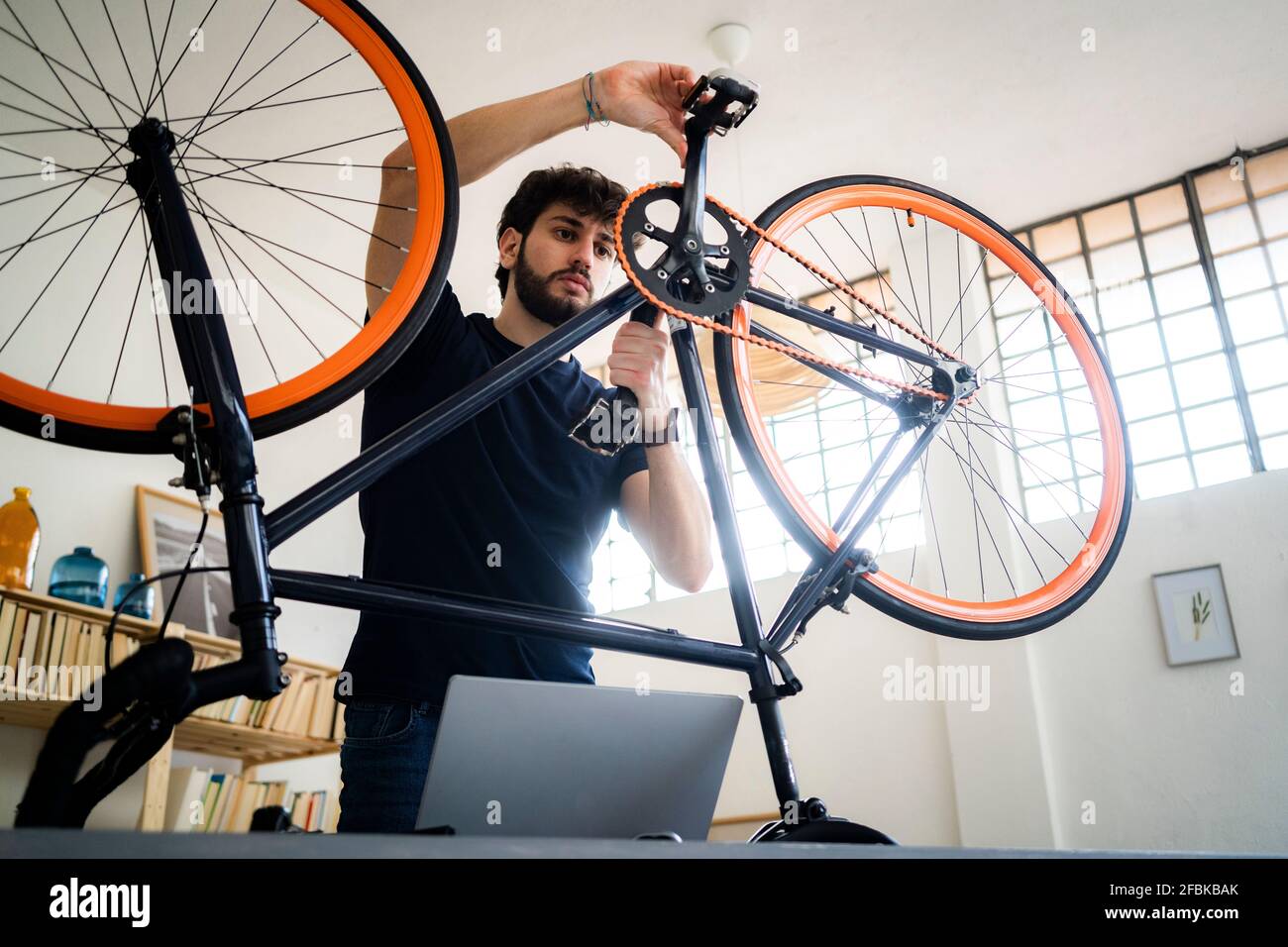 Man with laptop rotating bicycle pedals at home Stock Photo