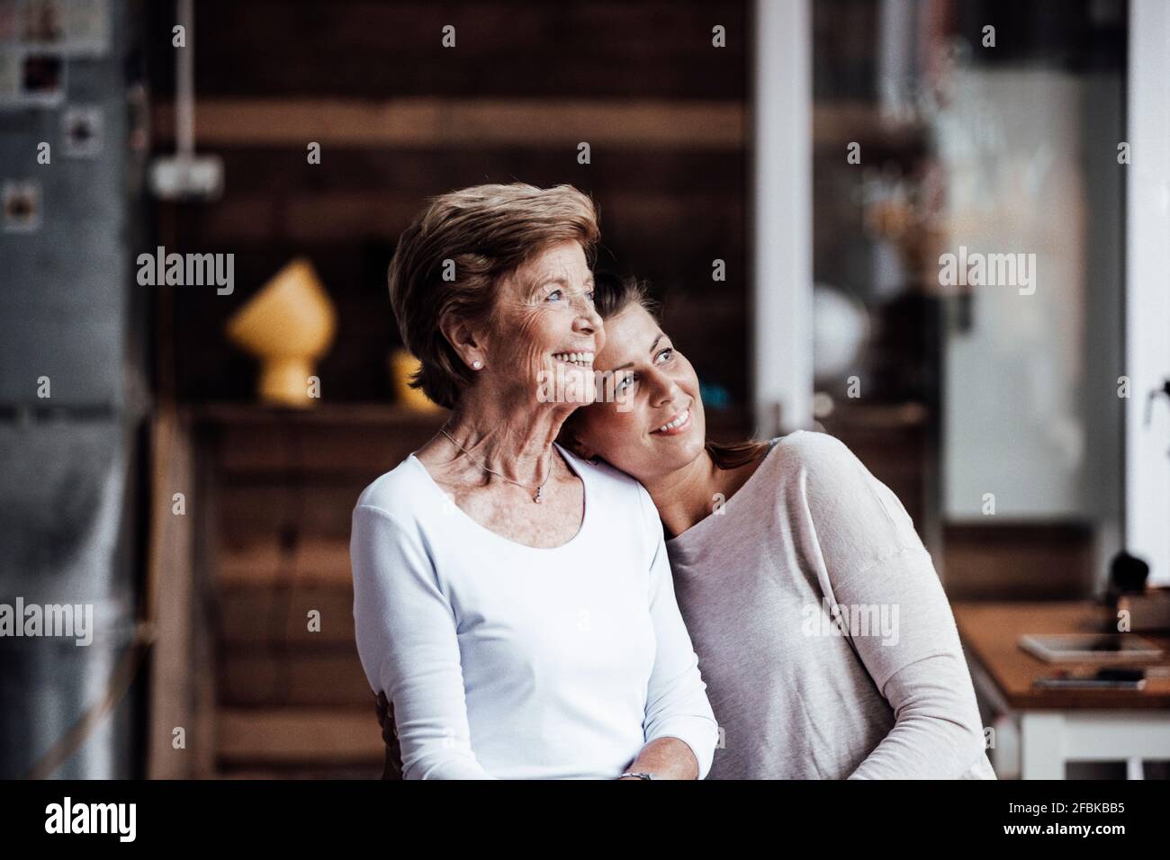 Smiling woman with head on shoulder of grandmother looking away Stock Photo