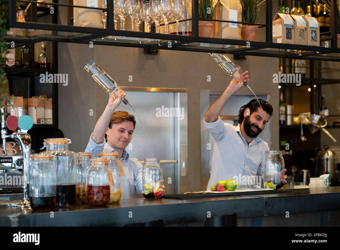 Handsome bartender and trainee pouring alcohol in fruit jar at bar