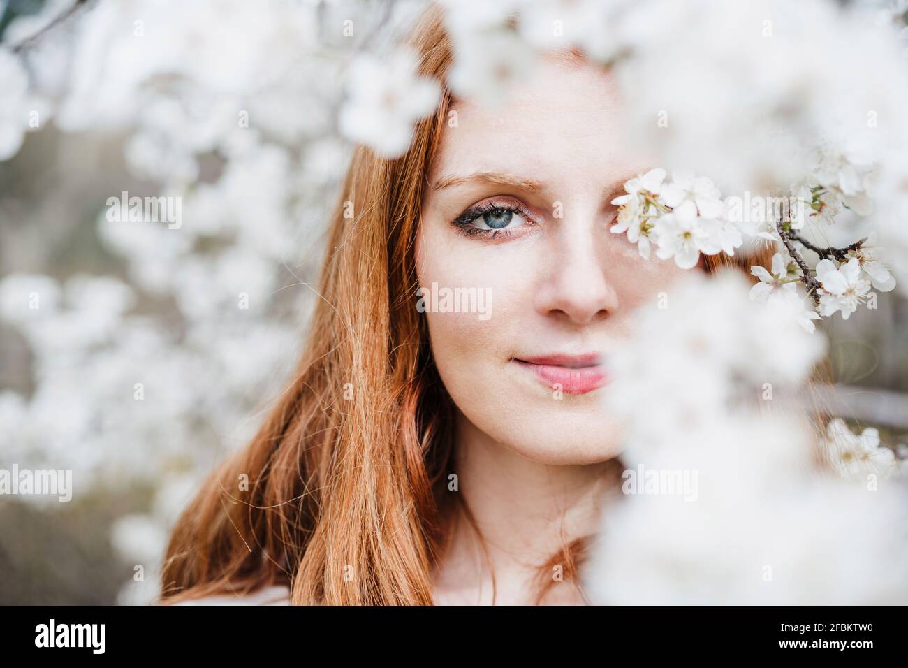 Beautiful young woman with gray eyes amidst white almond tree Stock Photo