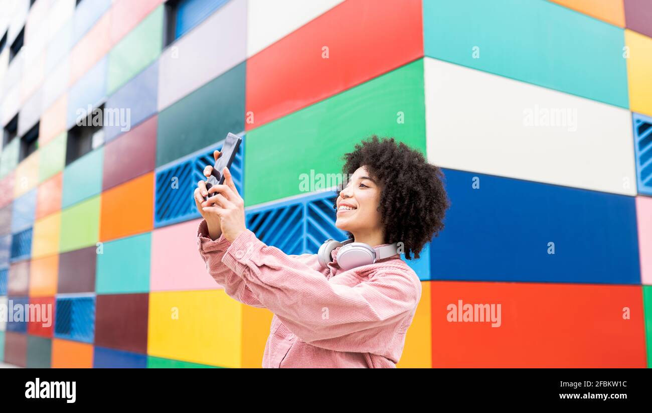Curly hair woman taking selfie by multi colored building Stock Photo