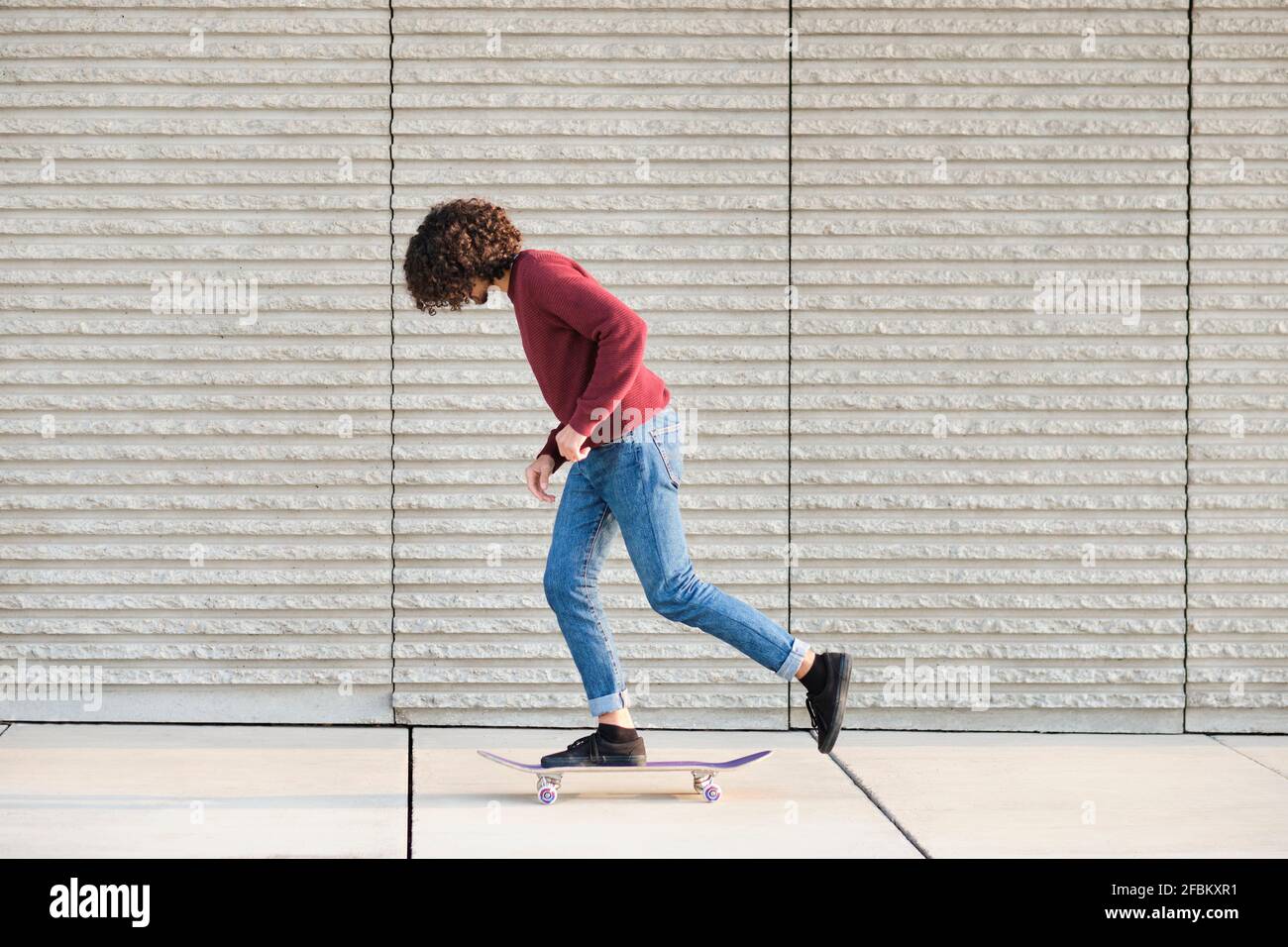 Curly haired man skateboarding by wall Stock Photo
