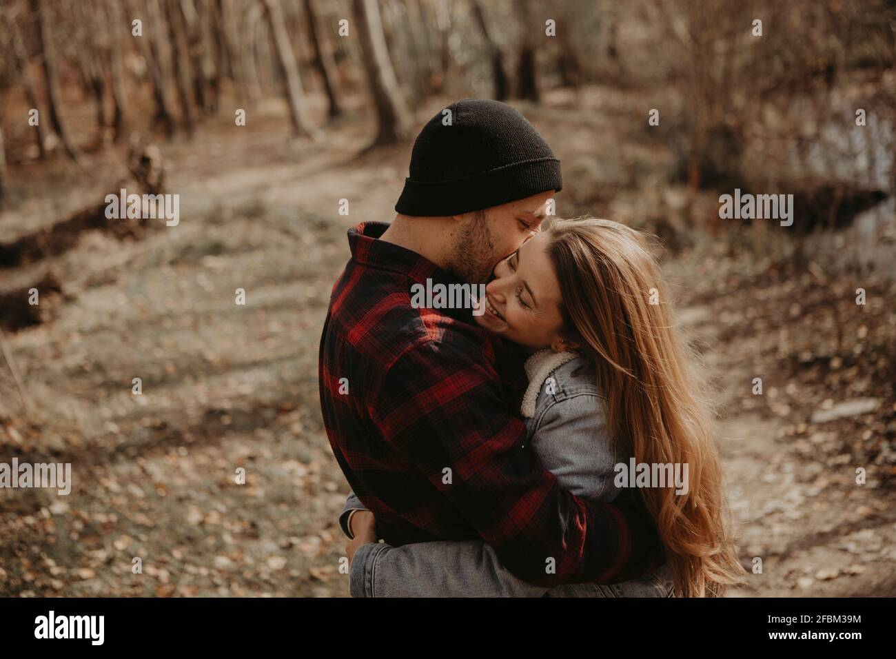 Woman in denim jacket kissing hipster boyfriend in forest during autumn ...
