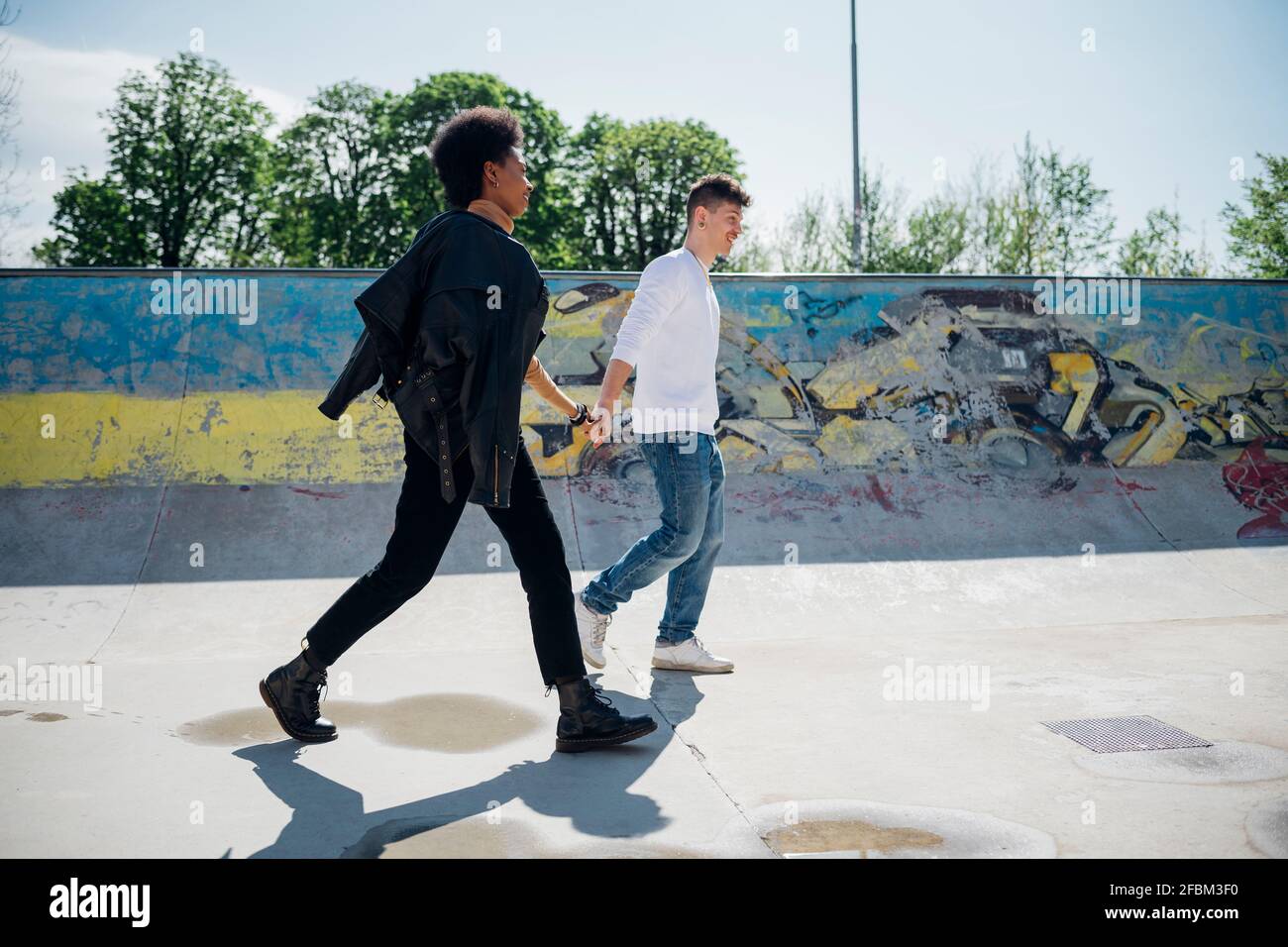 Multi ethnic couple holding hands while walking at skateboard park Stock Photo