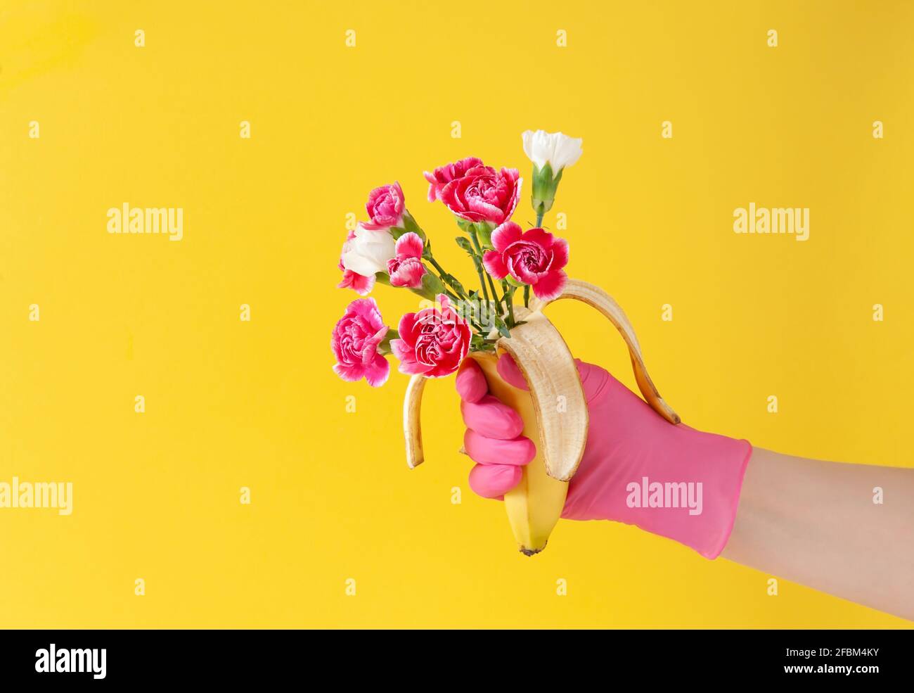 Creative arrangement with female hand in pink glove and  banana fruit with bouquet with colorful flowers over bright yellow background. Minimal  conce Stock Photo