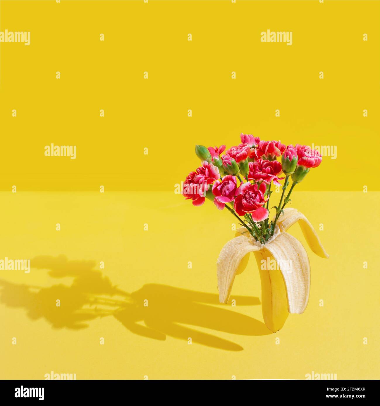Summer concept made with fresh banana fruit and red flowers over bright yellow background. Minimal sunlight summer concept with exclusive banana . Stock Photo