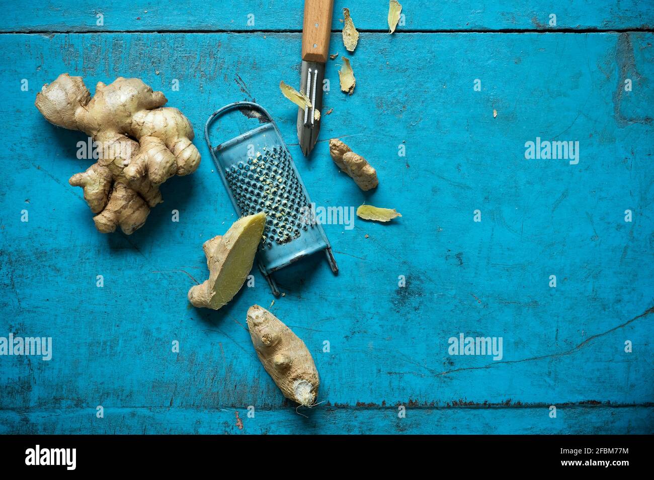 Ginger root, grater and kitchen knife lying on blue wooden surface Stock Photo