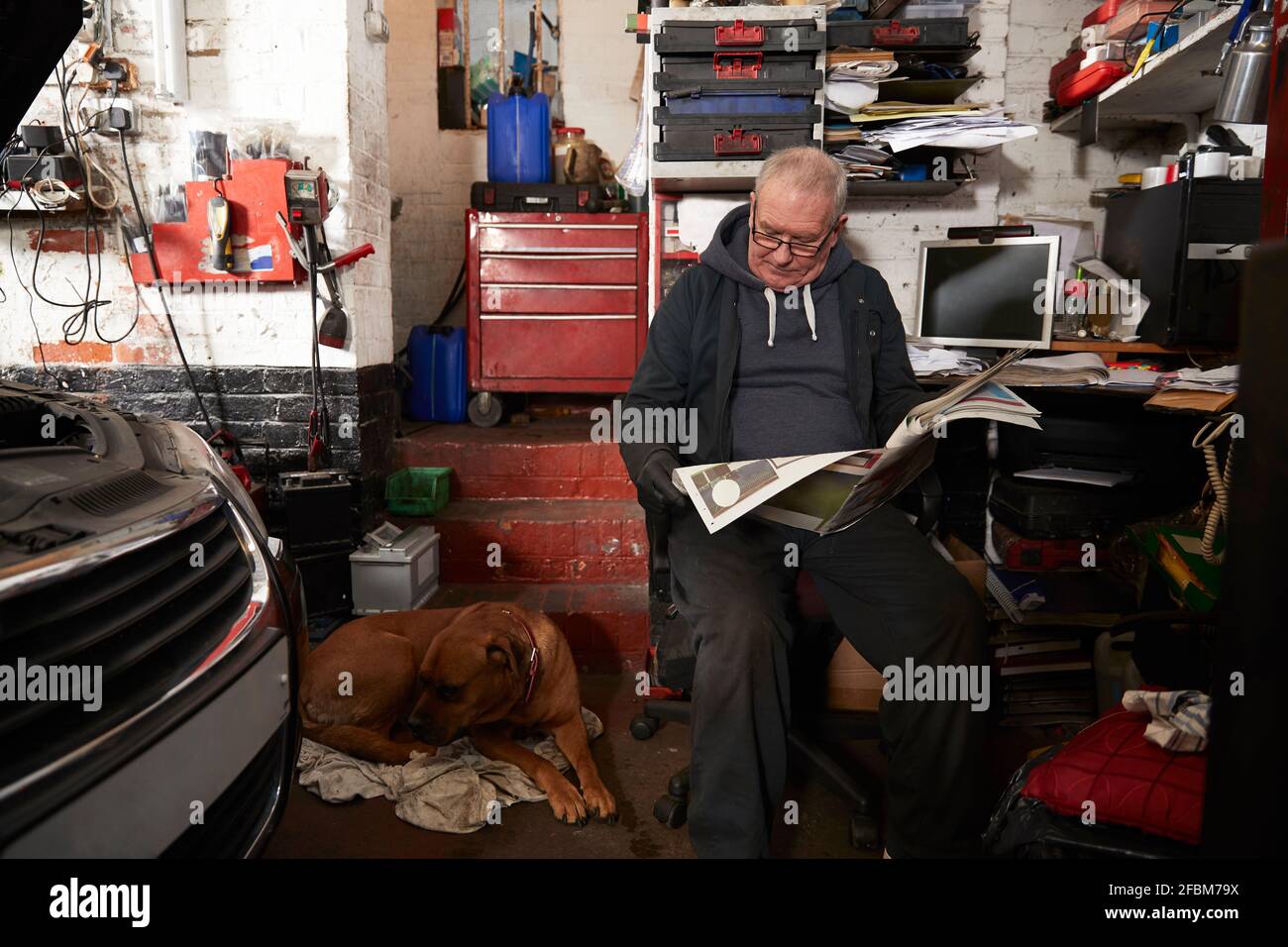 Senior male auto mechanic reading newspaper while sitting in garage
