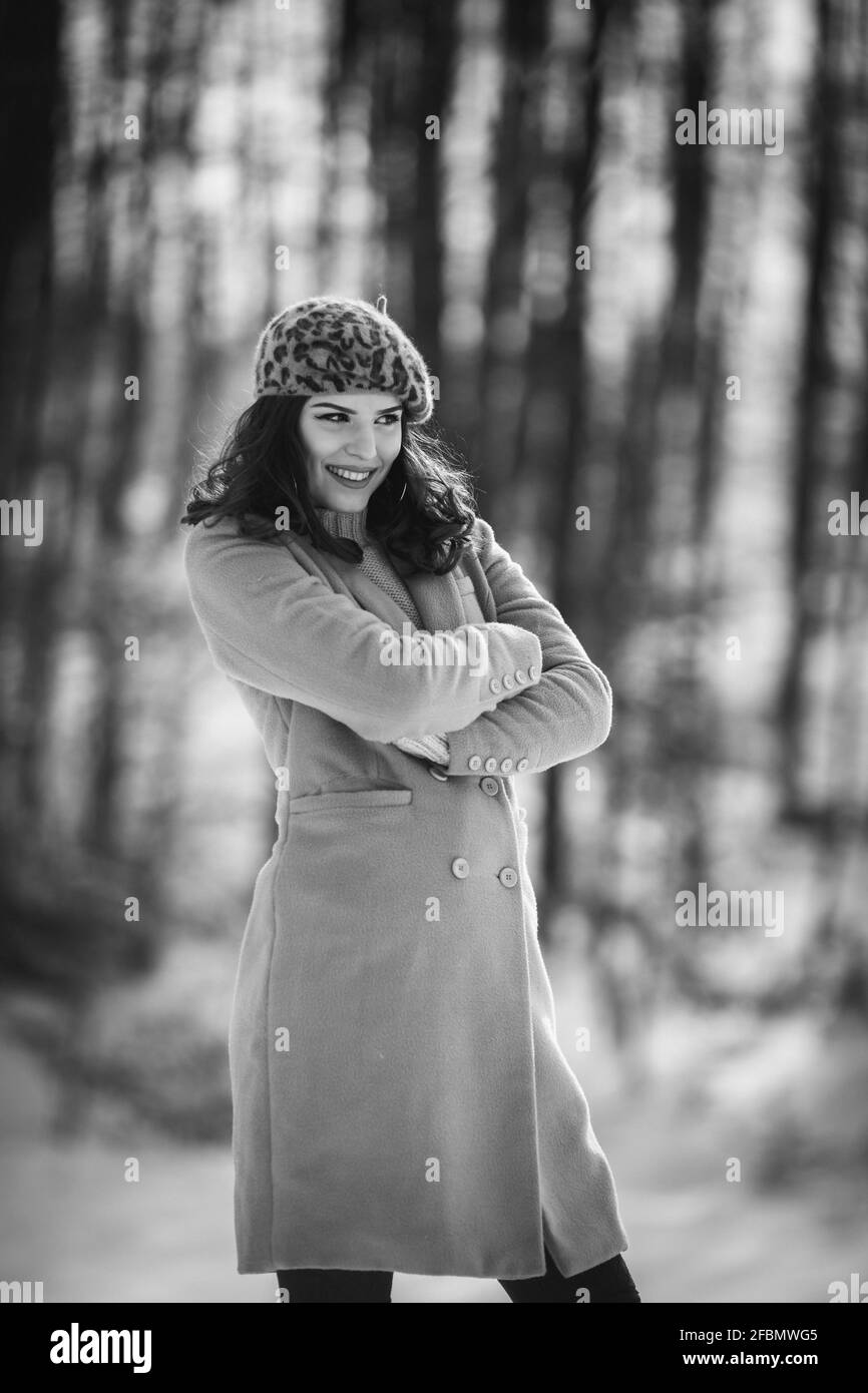 Grayscale shot of a Caucasian female wearing a coat in a park with trees covered in snow Stock Photo