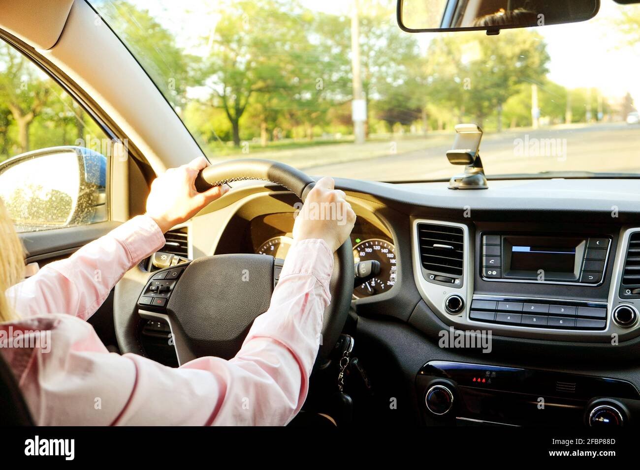 Close up of young woman hands holding steering wheel while driving car. Dashboard panel, phone holder mount, windshield. Businesswoman man inside vehi Stock Photo