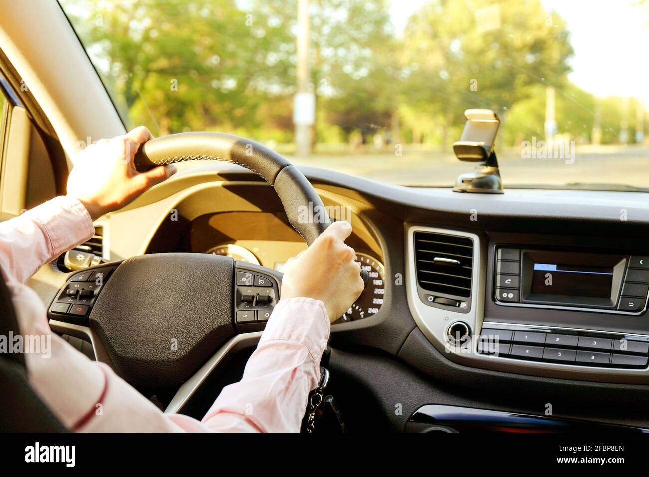 Close up of young woman hands holding steering wheel while driving car. Dashboard panel, phone holder mount, windshield. Businesswoman man inside vehi Stock Photo
