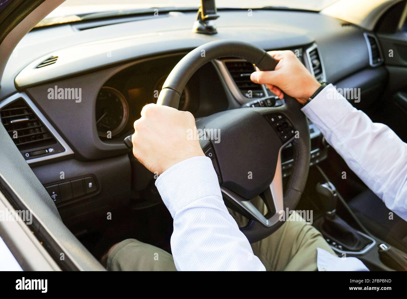 Close up of young man hands holding steering wheel while driving car. Dashboard panel, phone holder mount, windshield. Male business man inside vehicl Stock Photo