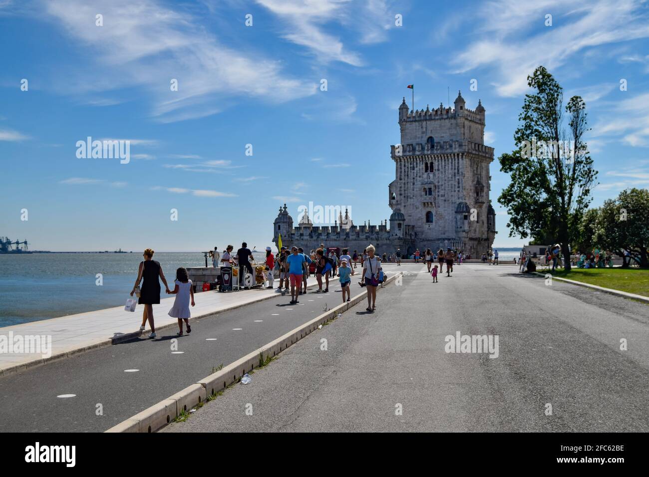 Walking in Lisbon to Belem tower of Saint Vincent, torre de Belém in Lisboa Portugal with tourists walking on the sidewalk. Portuguese Explorers Monuments Stock Photo