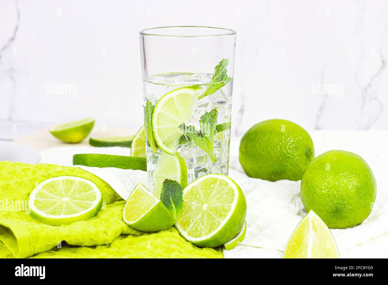 Fresh homemade mojito cocktail drink made from limes and mint leaves in a glass with ice cubes on light background in the kitchen. Stock Photo