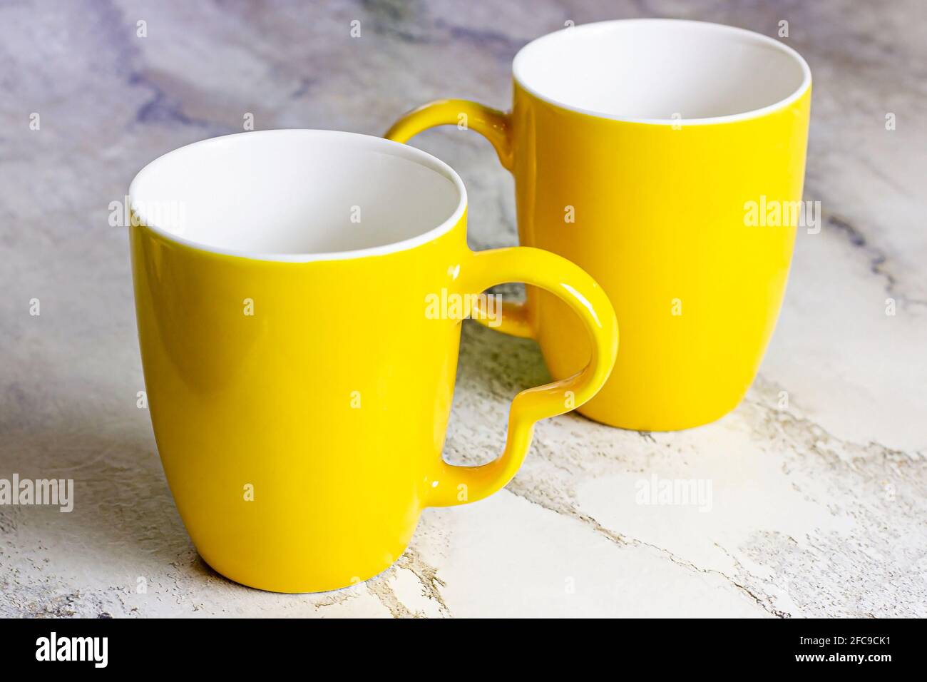 Two bright yellow empty tea cups on marble kitchen table background. Stock Photo