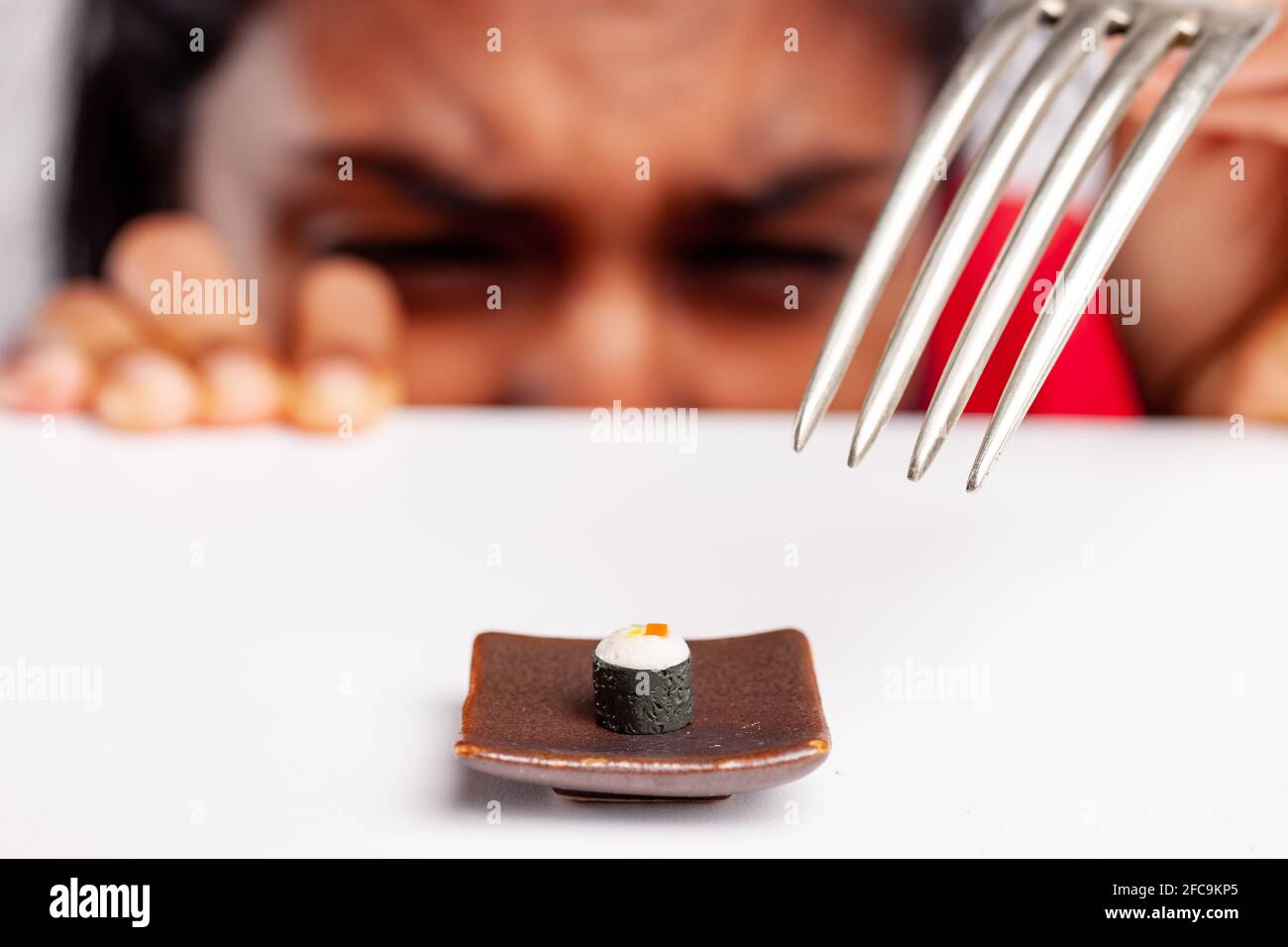 Woman eyeing sushi on a plate with disgust as she prepares to fork them in a fun food concept with miniature toy food and selective focus to the seafo Stock Photo