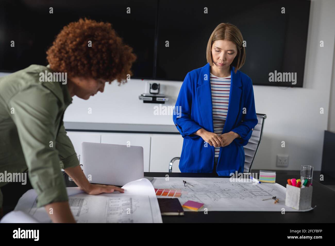 Diverse male and female colleagues in office discussing over blueprint ...