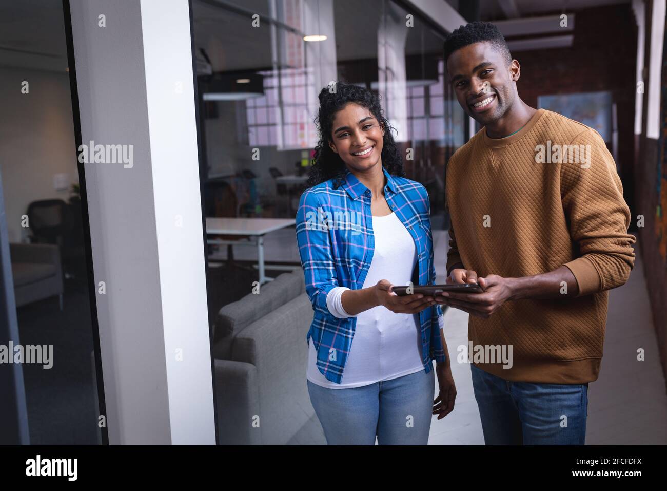 Happy diverse male and female colleagues at work discussing over tablet ...