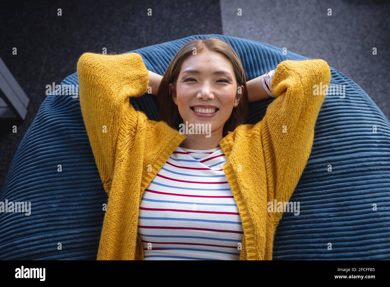 Happy mixed race businesswoman chilling in office relaxing space lying in beanbag smiling Stock Photo