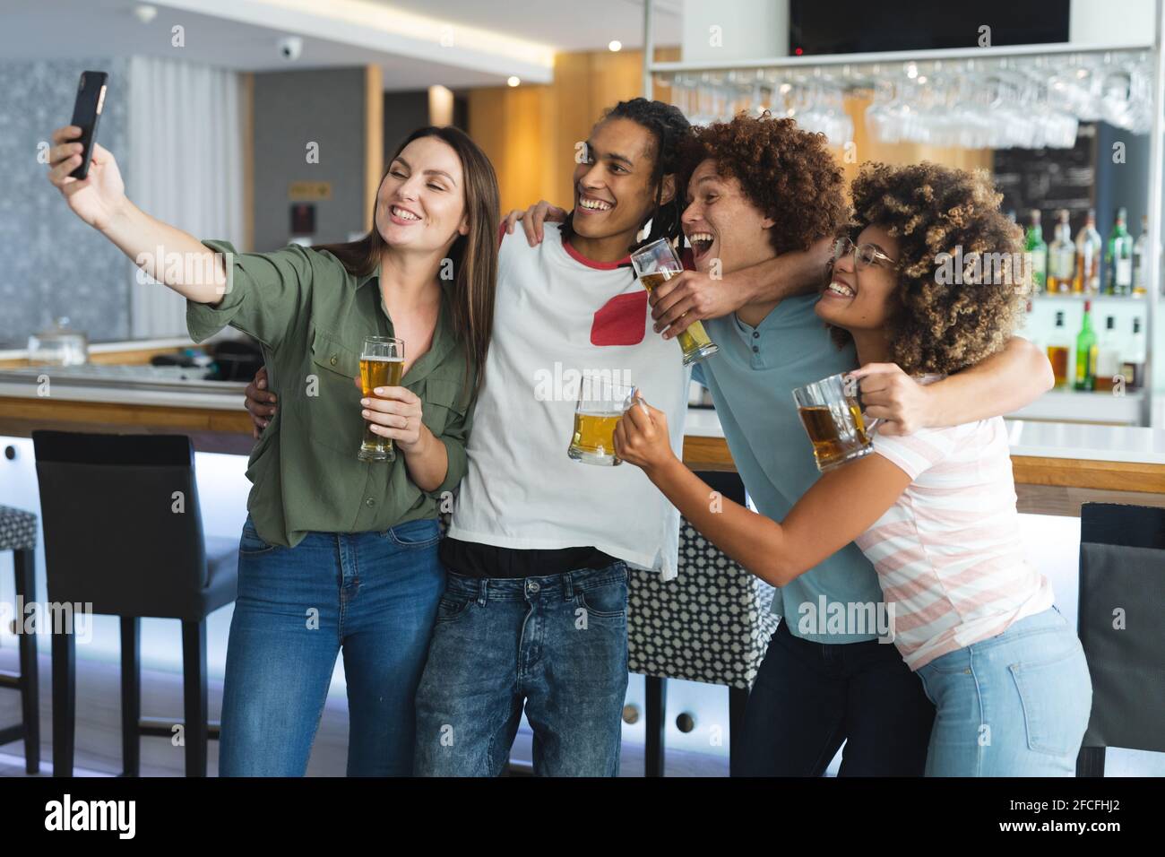 Diverse group of male and femalefriends raising glasses and taking selfie at bar Stock Photo