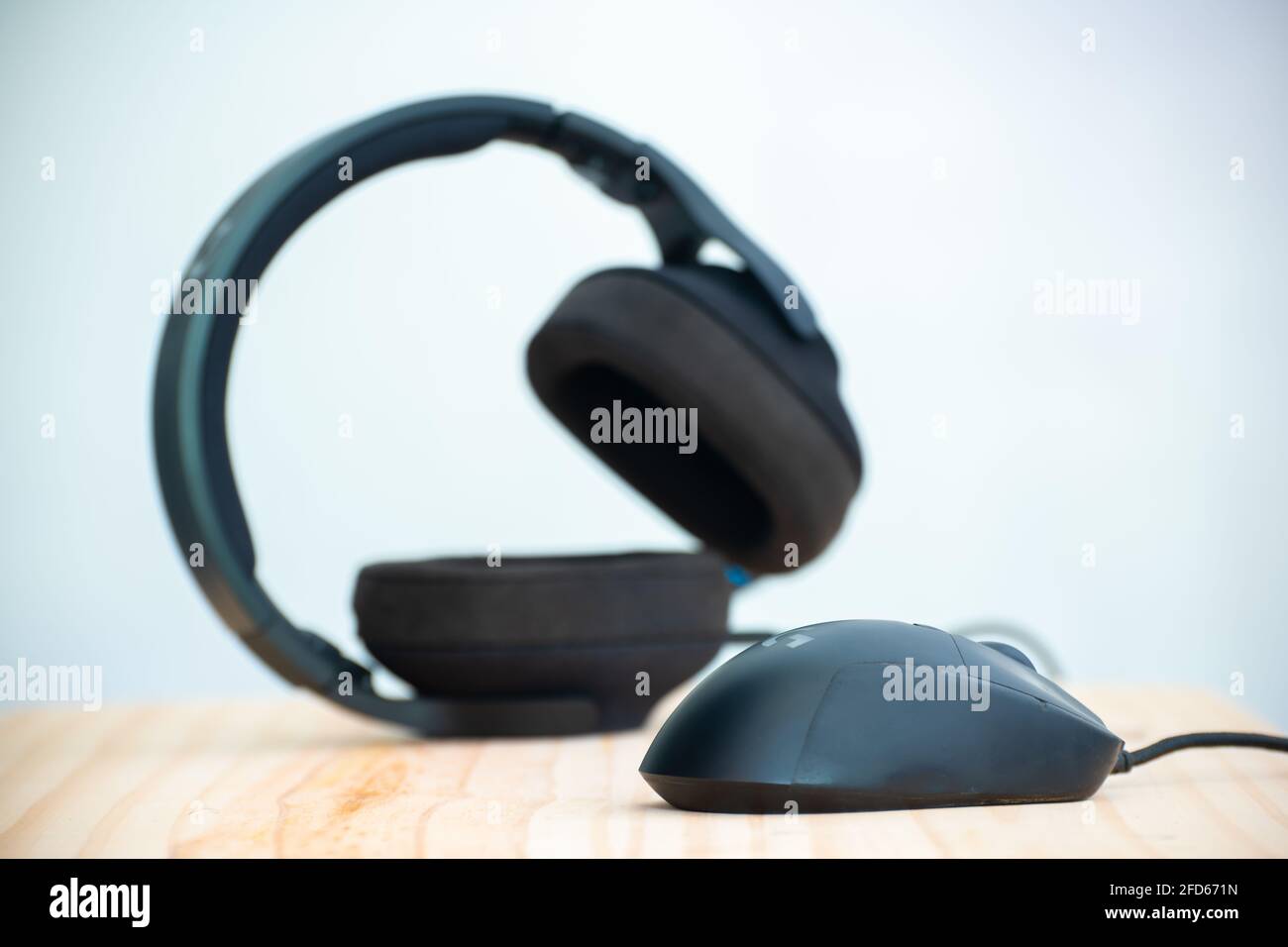 Headphone and the mouse in a wooden computer table, mouse in focus as headset blurred behind, darker objects against the lighter background photograph Stock Photo