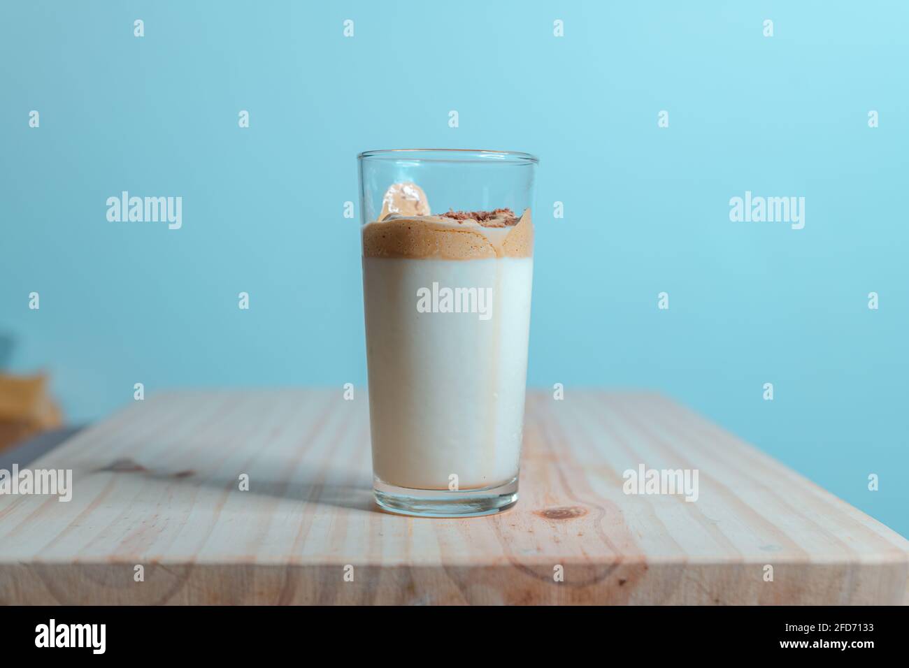 Homemade Dalgona coffee glass in a wooden textured tabletop. whisked instant coffee topping with fresh milk, making the delicious Korean drink. Trendy Stock Photo